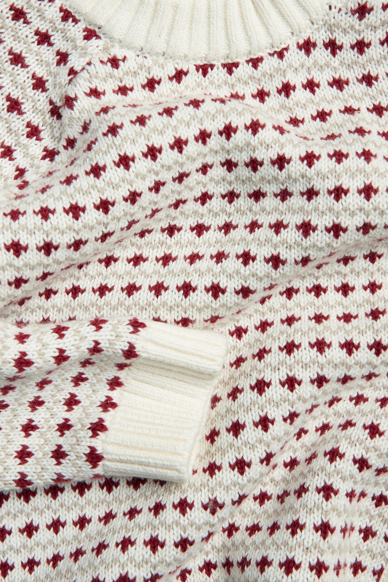 Nahaufnahme eines off-white gestrickten Baumwollpullovers mit rot-beigem Jacquardmuster und Rippenbündchen.