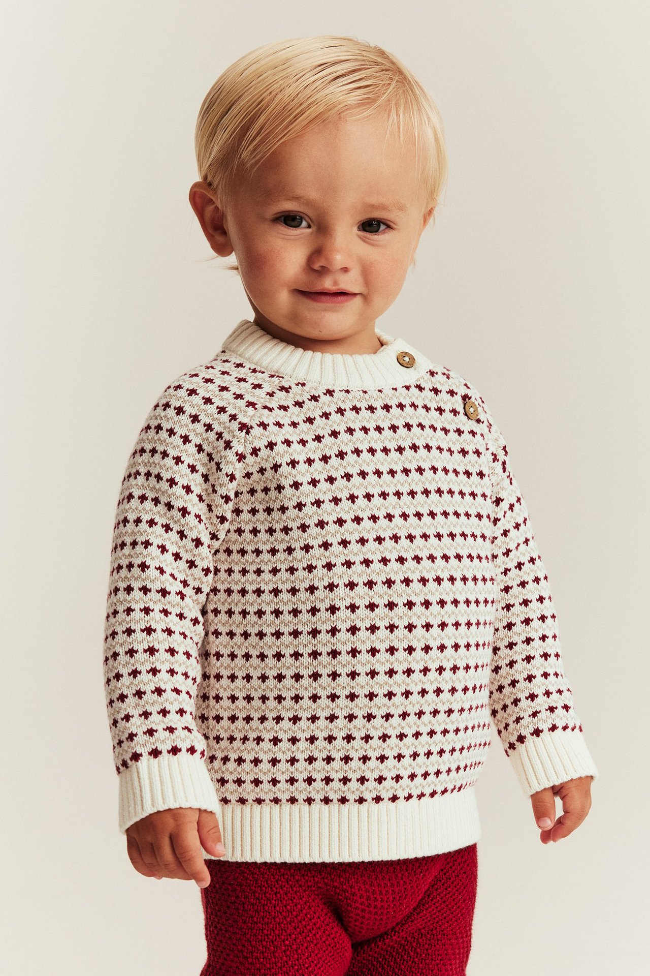 Child in offwhite knitted sweater with buttons, raglan sleeves, ribbed cuffs, jacquard pattern.