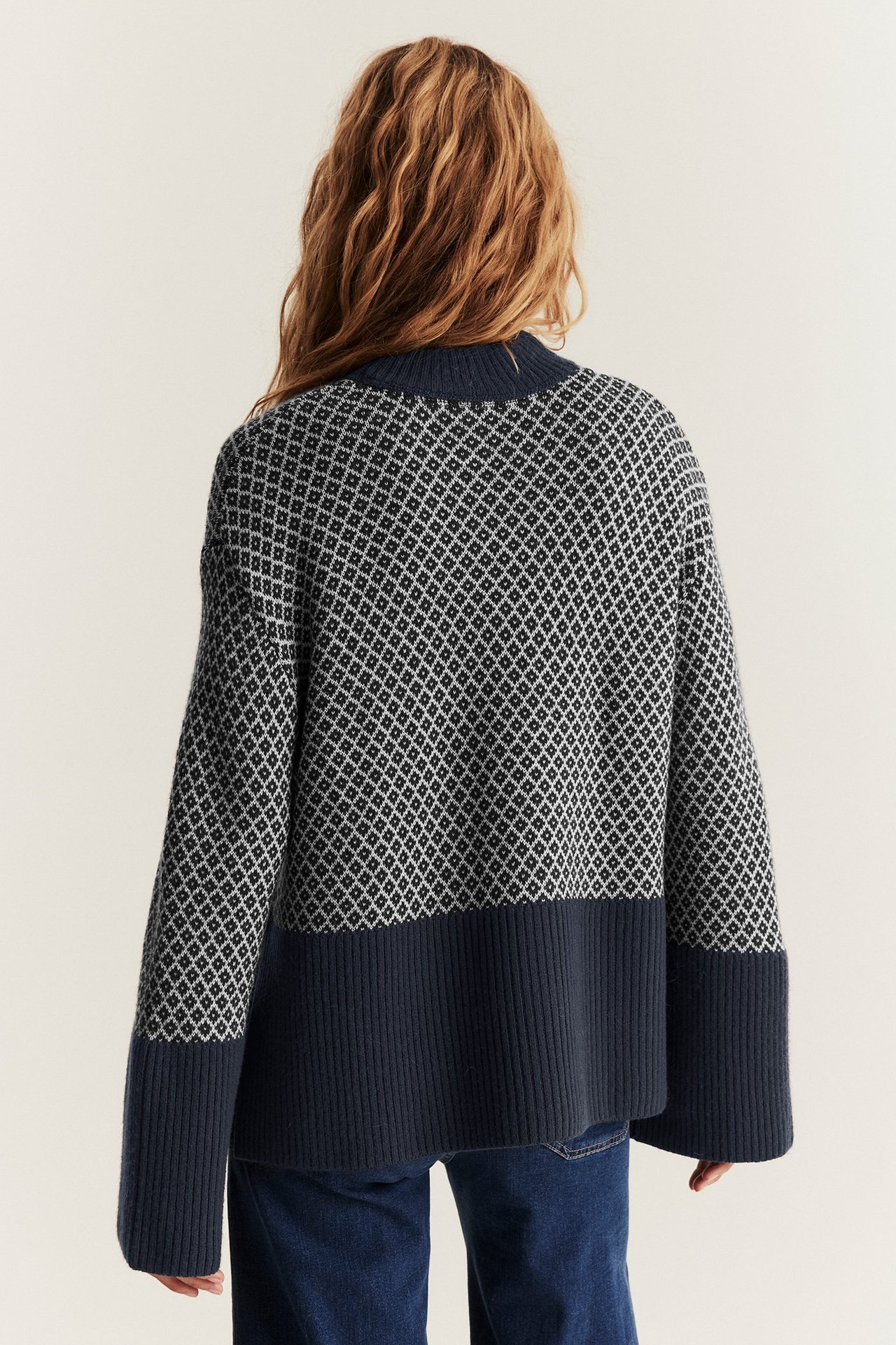 Rückenansicht einer Frau in dunkelblauem Jacquard-Wollpullover mit weiten Ärmeln und dunkelblauen Jeans.