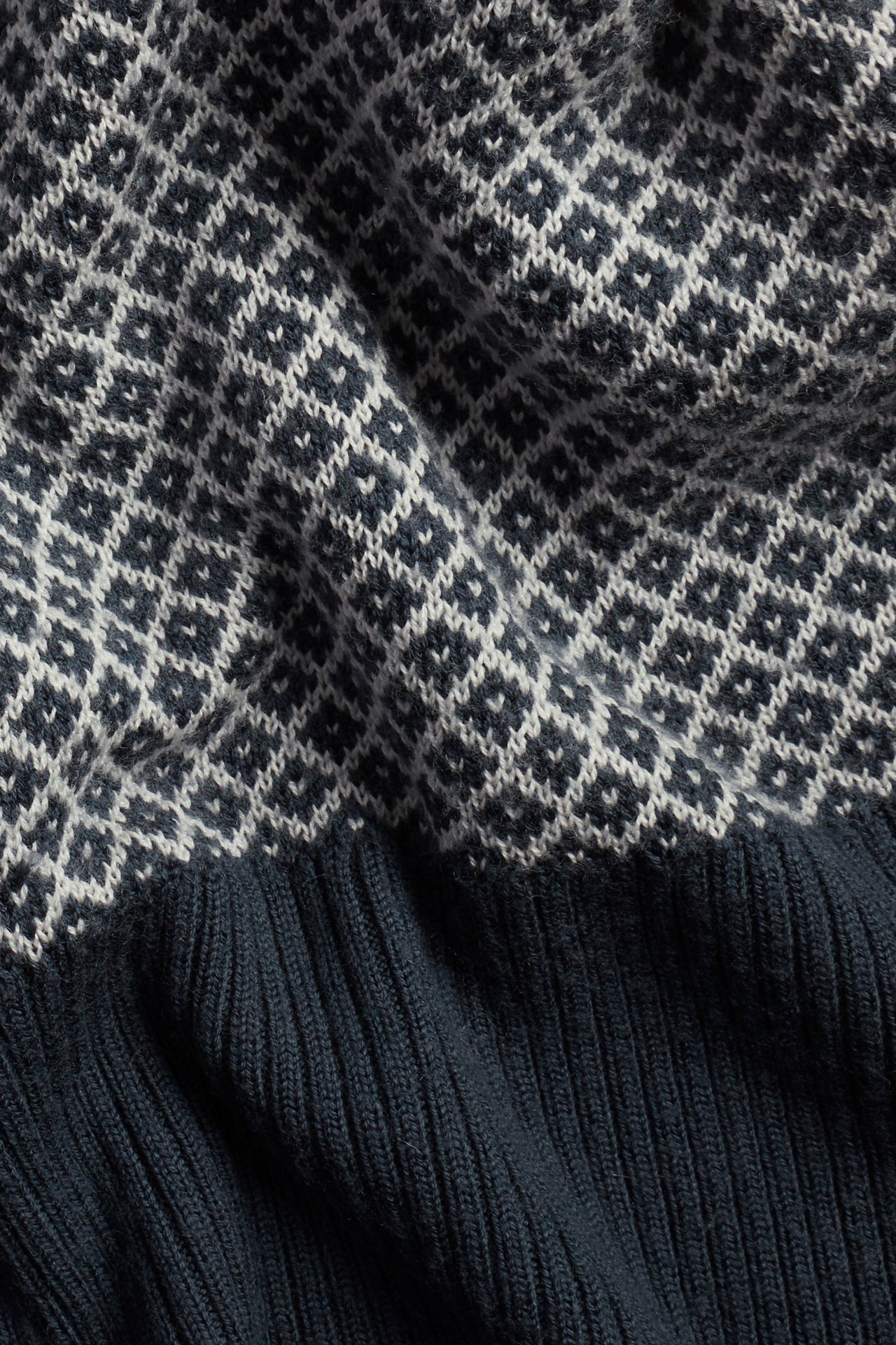Nahaufnahme eines dunkelblauen Wollpullovers mit weißem Jacquardmuster und geripptem Saum.
