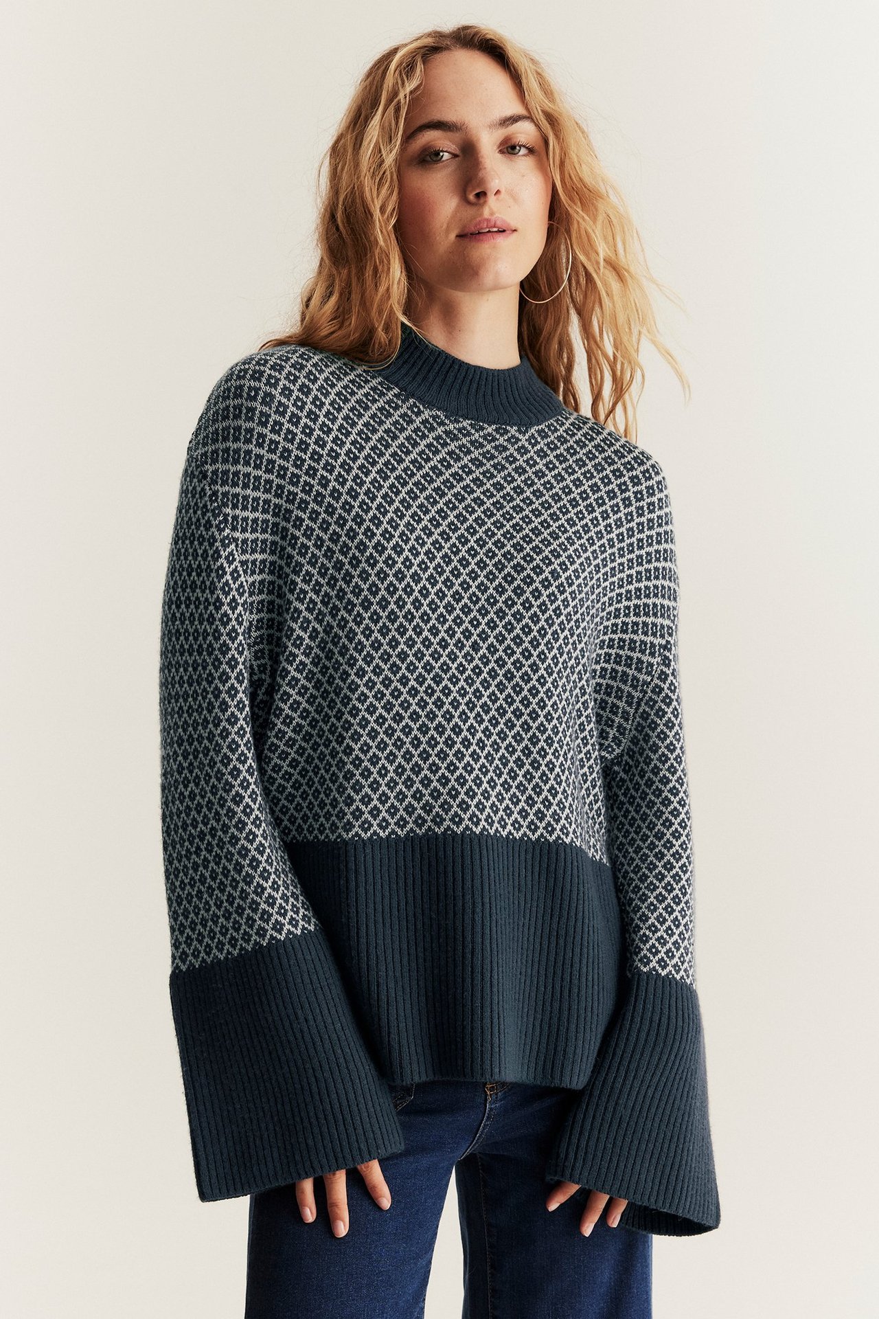 Frontansicht einer Frau in dunkelblauem Jacquard-Wollpullover mit weiten Ärmeln und dunkelblauen Jeans.