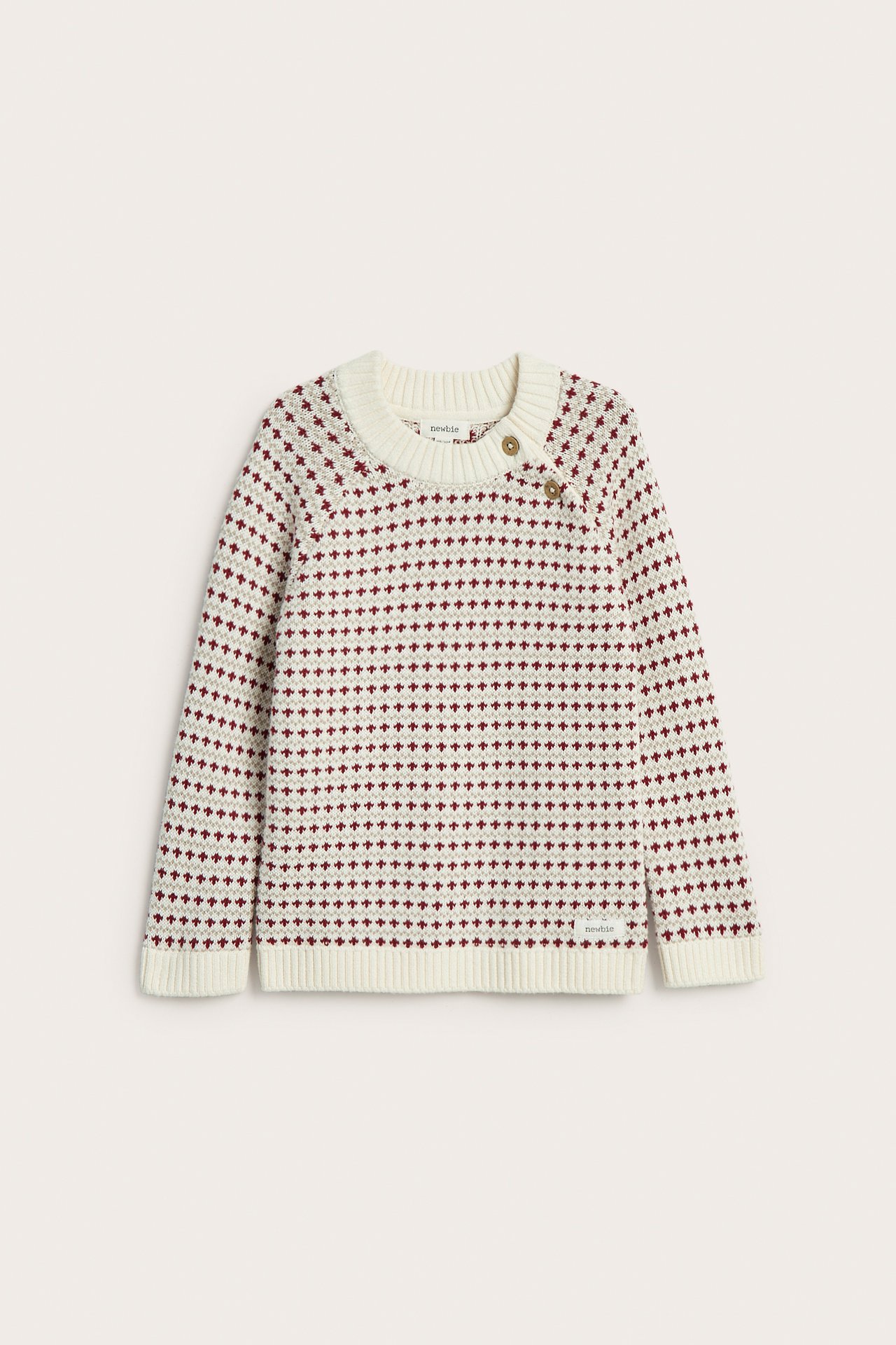 Vorderansicht: Kinder-Strickpullover aus cremeweißer Baumwolle mit rotbraunem Jacquardmuster, zwei Knöpfe an der Schulter.