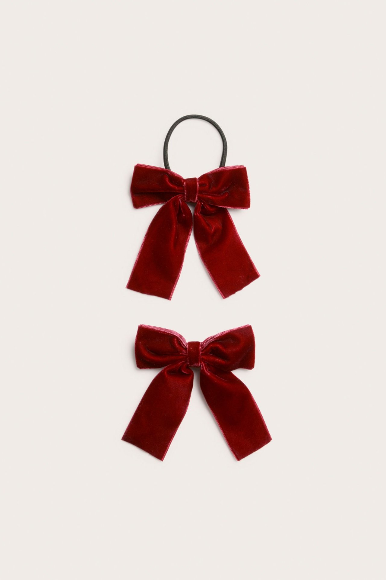 Close-up of two red velvet hair bows, one with a black elastic tie, one with a clip.