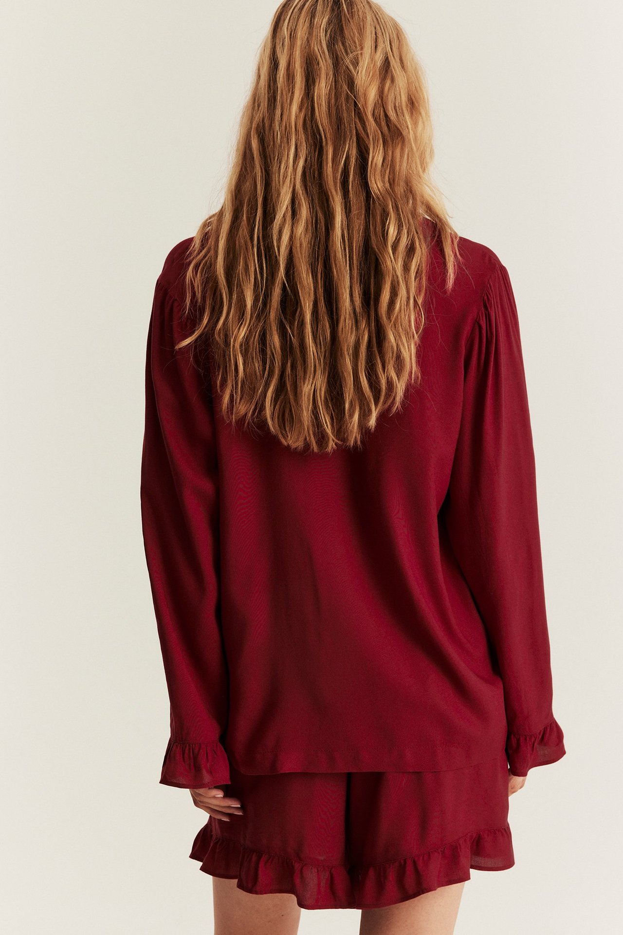 Back view of a woman in a red woven viscose pyjamas set: long-sleeved shirt and frilled shorts.