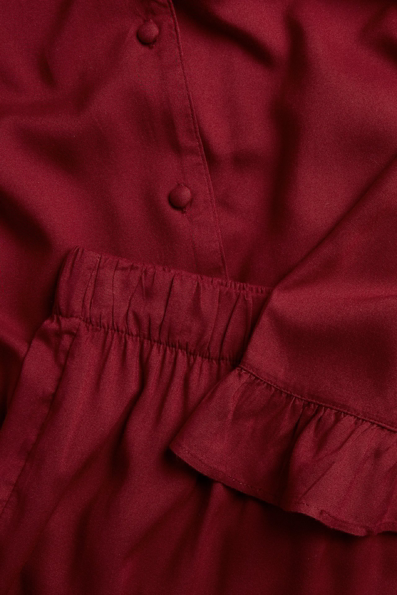Nahaufnahme eines roten gewebten Viskose-Damenpyjamas: geknöpftes Oberteil mit Rüschenmanschetten, Shorts mit Gummibund.
