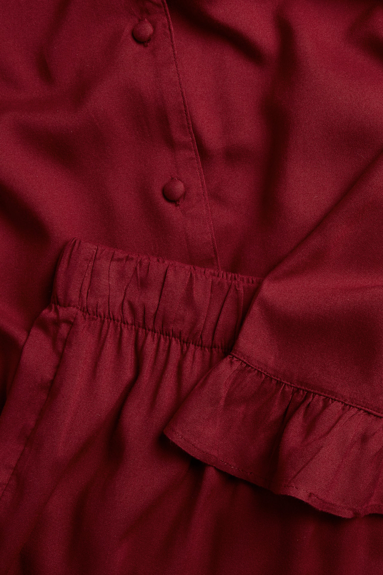 Nahaufnahme eines roten gewebten Viskose-Damenpyjamas: geknöpftes Oberteil mit Rüschenmanschetten, Shorts mit Gummibund.