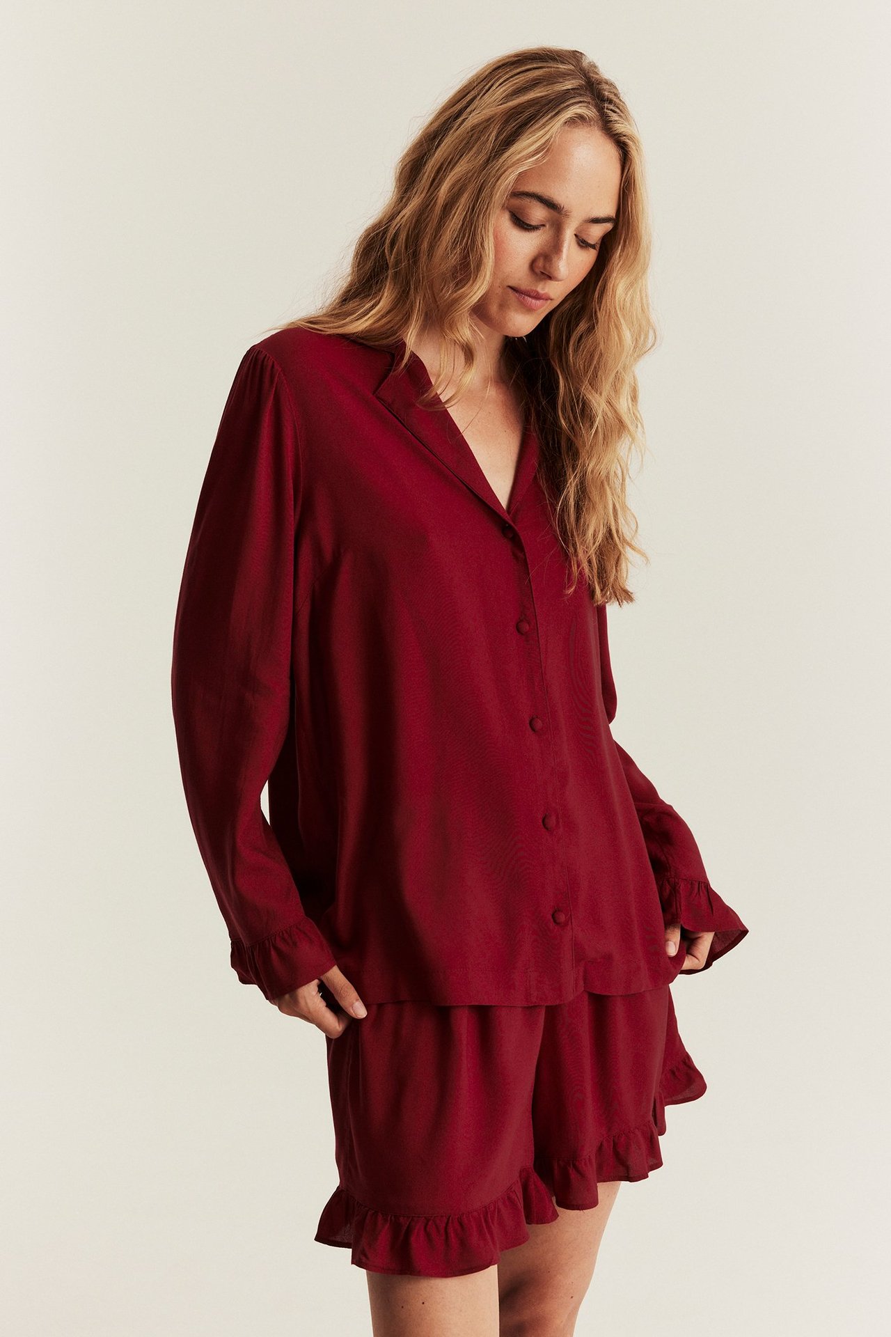 Front view: Woman in a red viscose pajama set, collared shirt with ruffles and matching ruffled shorts.
