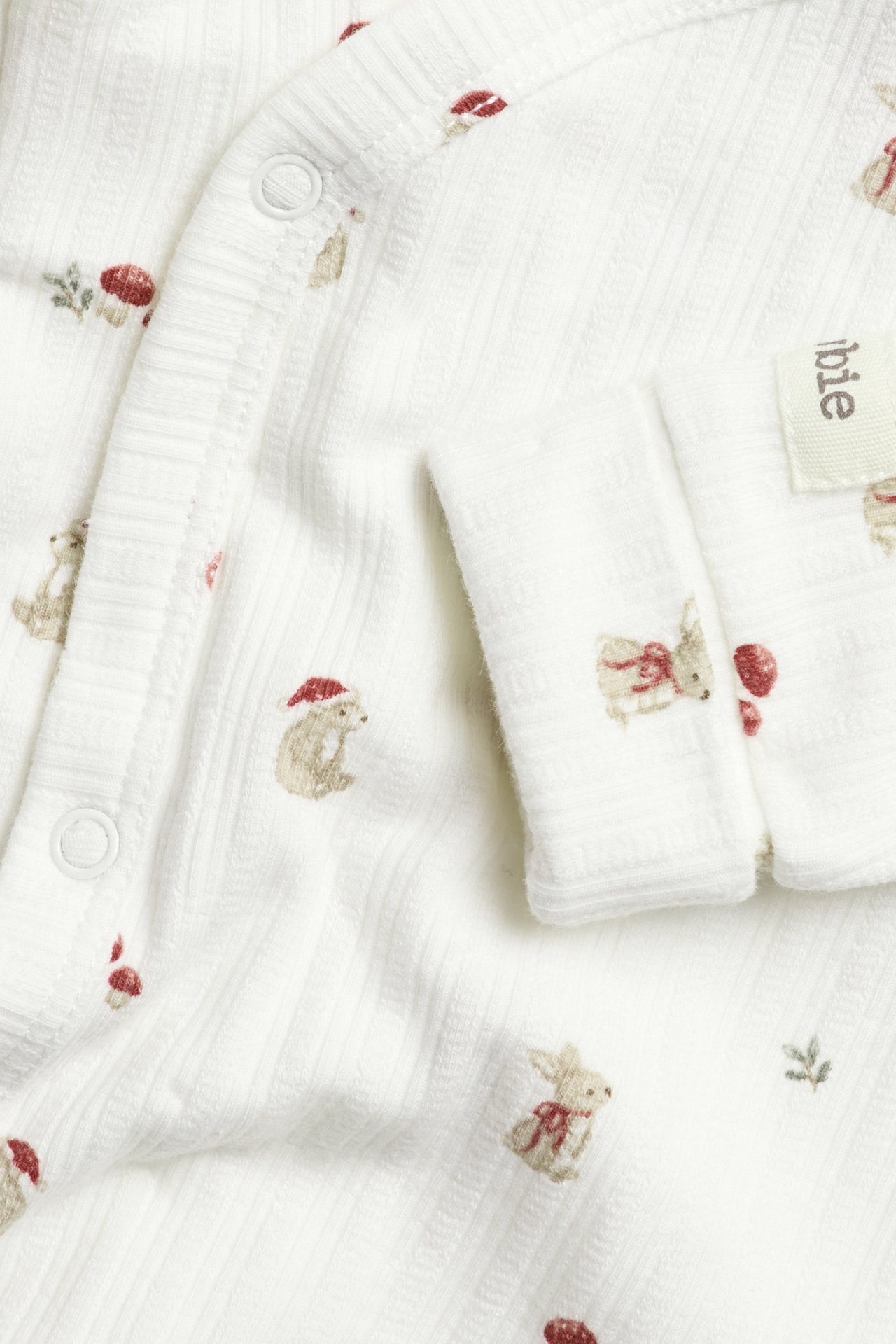 Nahaufnahme eines cremefarbenen Baby-Wickelbodys mit Tiermuster, Druckknöpfen und gerippter Baumwolle.