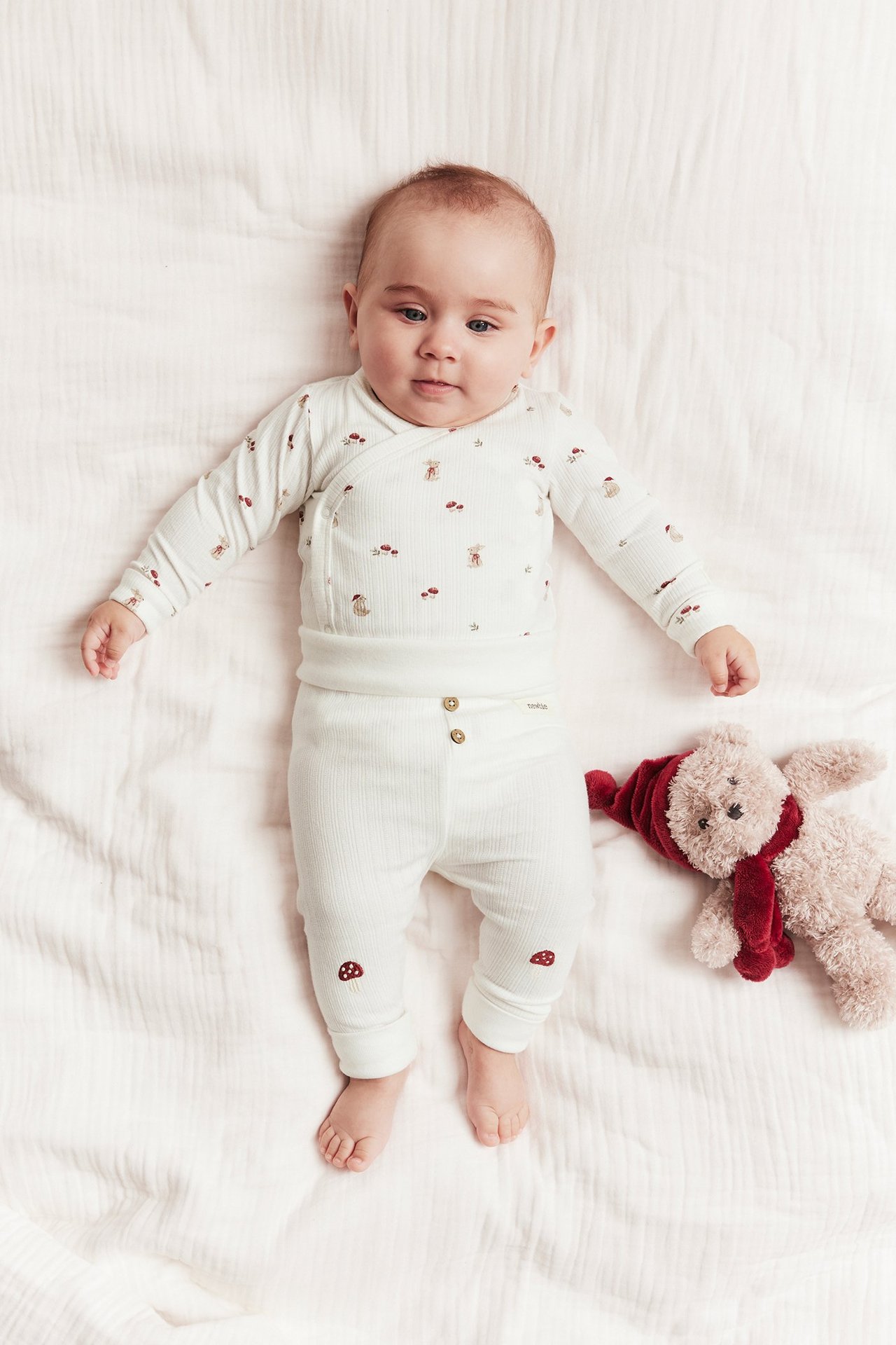 Von oben: Baby trägt cremeweißen gerippten Langarm-Wickelbody mit Tier/Pilzprint und passende Hose.