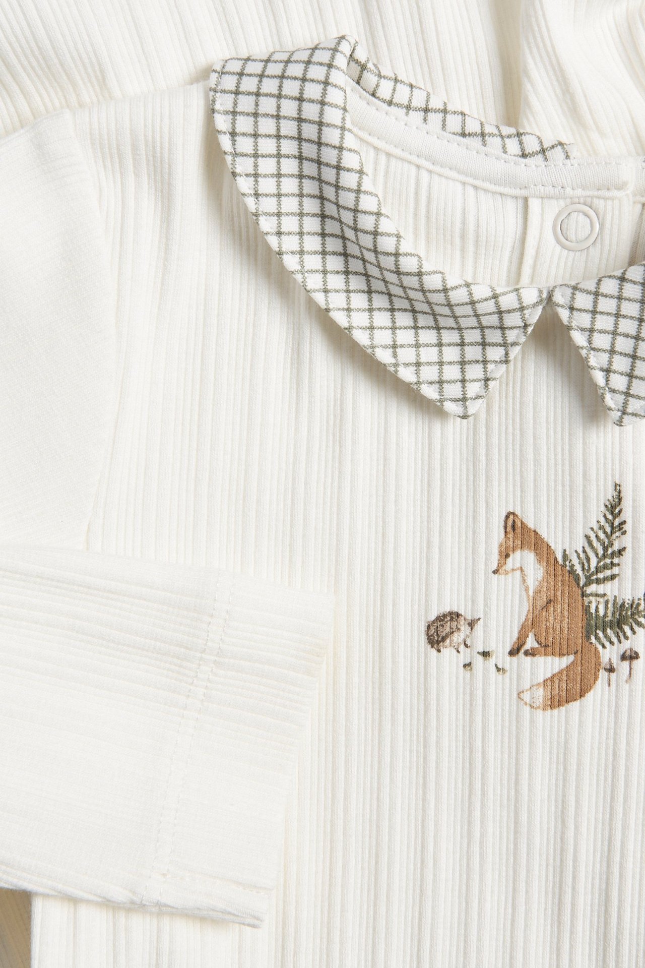 Nahaufnahme eines gerippten, cremefarbenen Baby-Bodys mit kariertem Kragen und Fuchsdruck vorne.
