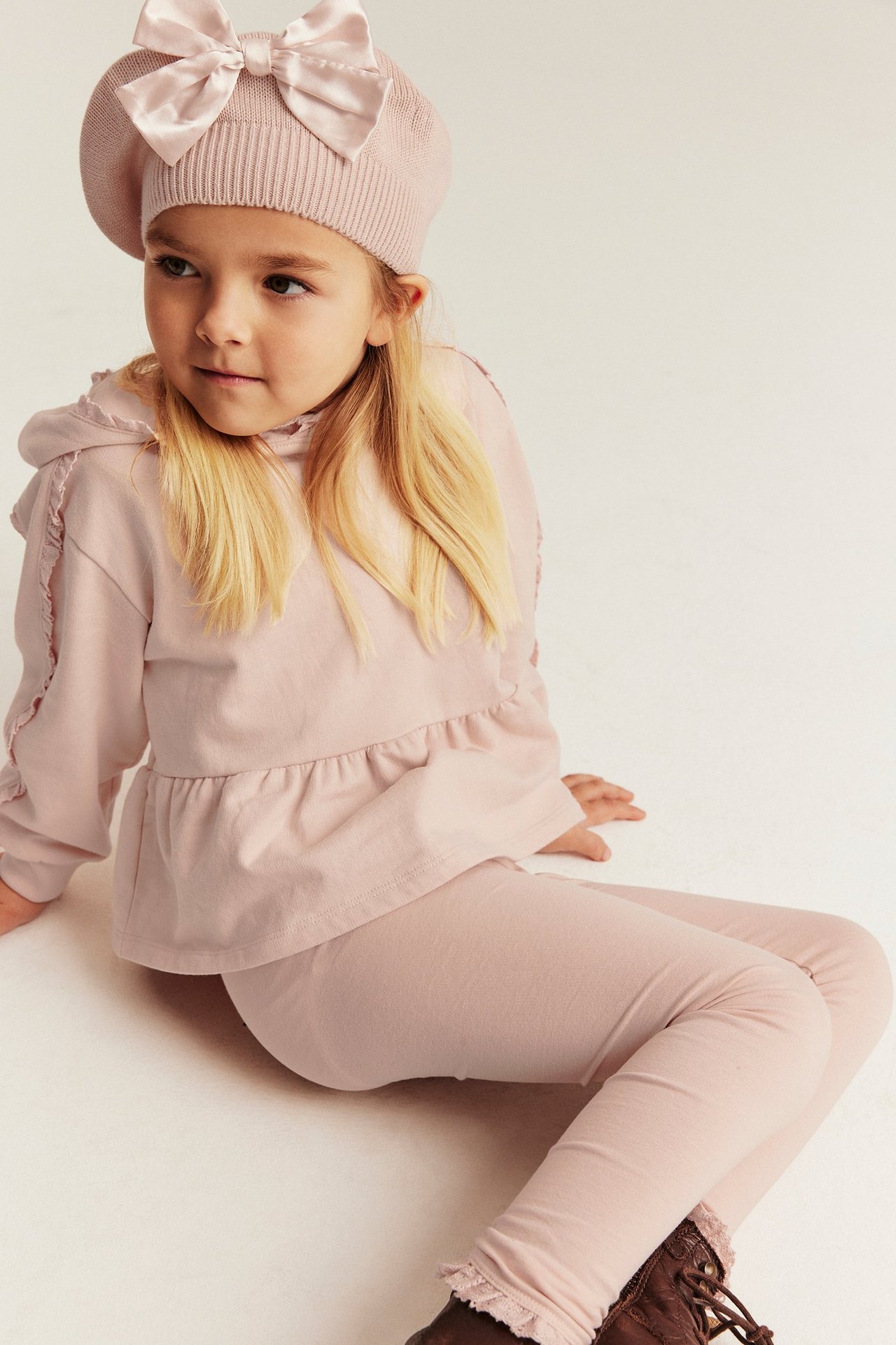 Vorderansicht: Mädchen trägt hellrosa Kapuzen-Sweatshirt mit Spitze, passende Leggings und rosa Baskenmütze mit Schleife.
