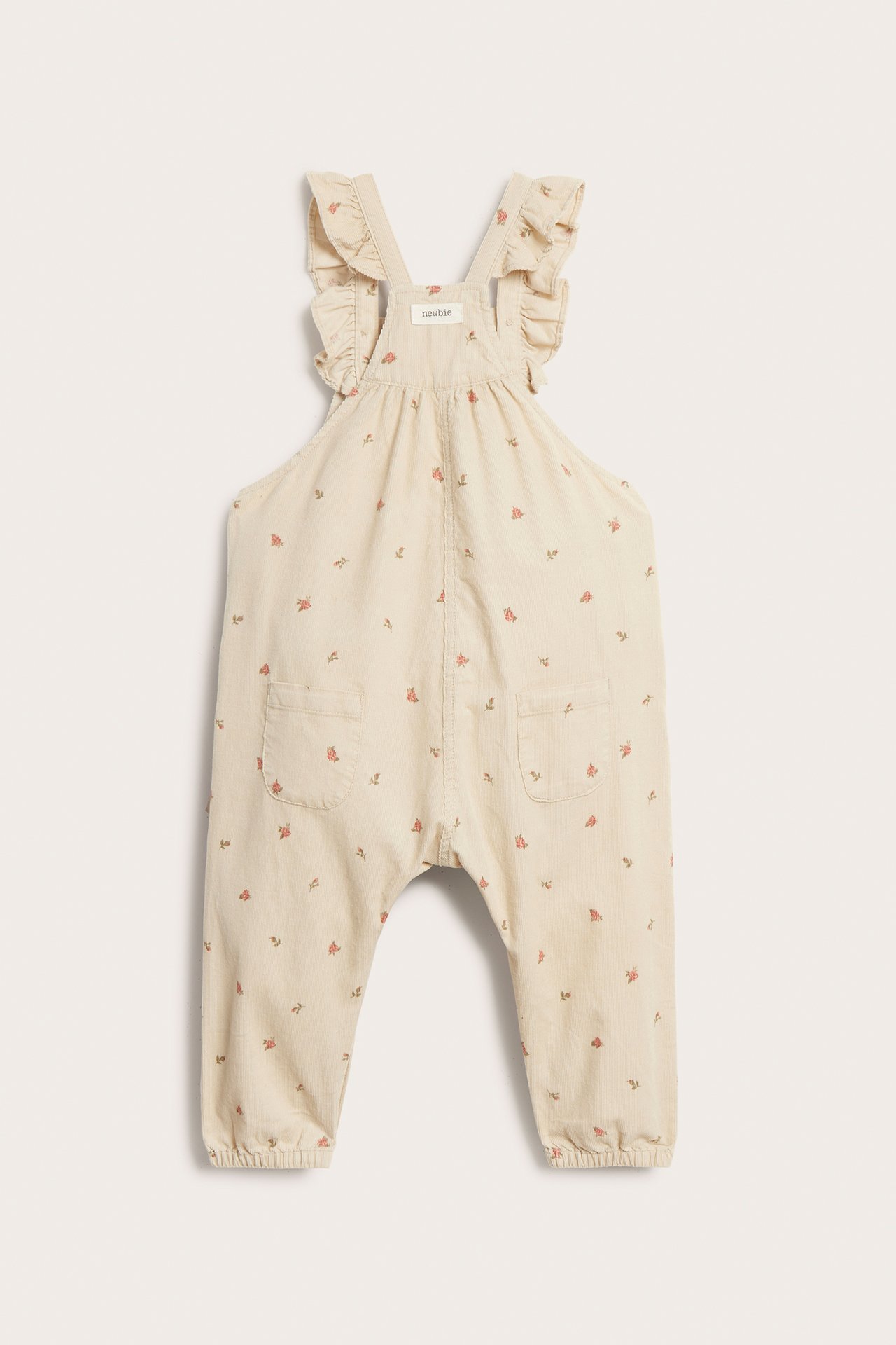 Front view of beige cotton corduroy overalls with floral pattern, ruffled straps, and front pockets.