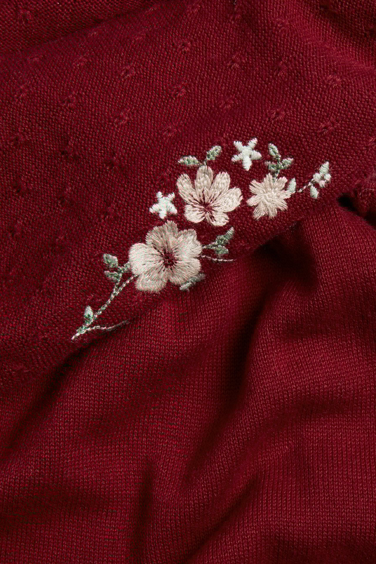 Close-up of a red knitted cotton dress with light beige floral embroidery.