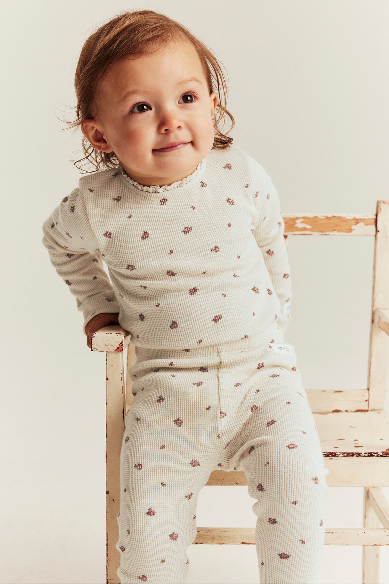 Front view: baby in light beige waffle knit floral bodysuit with lace trim and matching leggings.