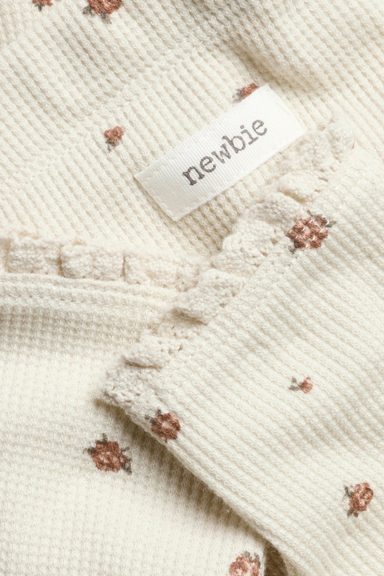 Nahaufnahme: Hellbeige Waffelstrick-Leggings mit kleinem braunem Blumenmuster, Spitzenbesatz und Newbie-Etikett.