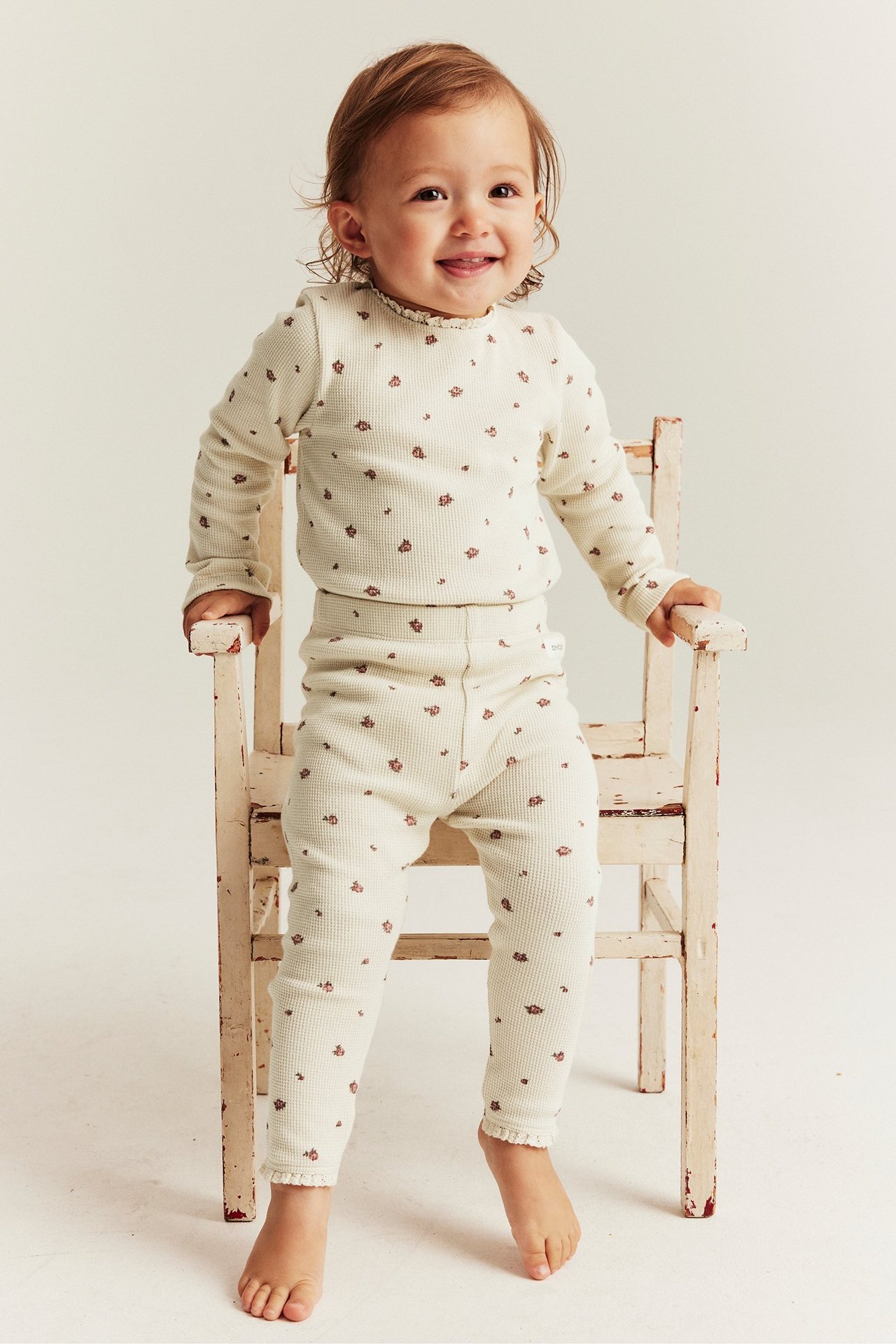 Vorderansicht: Baby trägt hellbeige Waffelstrick-Leggings mit kleinem Blumenmuster und passendem Oberteil.