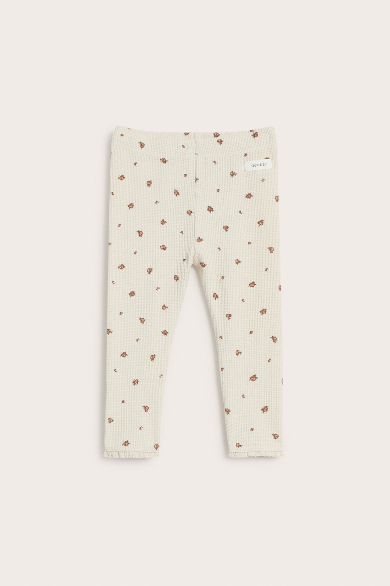 Vorderansicht von hellbeigen Waffelstrick-Baby-Leggings mit kleinem Blumenmuster und Rüschen an den Beinabschlüssen.