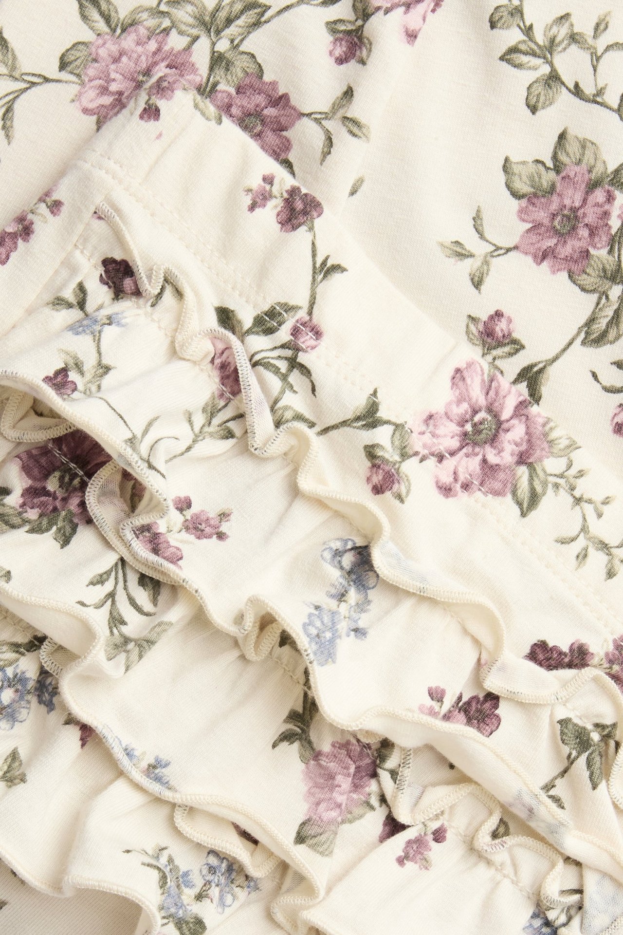 Nahaufnahme von hellbeigen floralen Leggings mit lila und blauen Blumen und Rüschen.