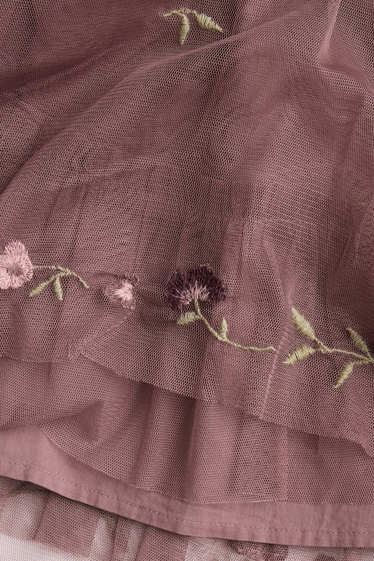 Nahaufnahme eines dunkelrosa Mesh-Kleides mit gestickten rosa und lila Blumen und grünen Blättern.