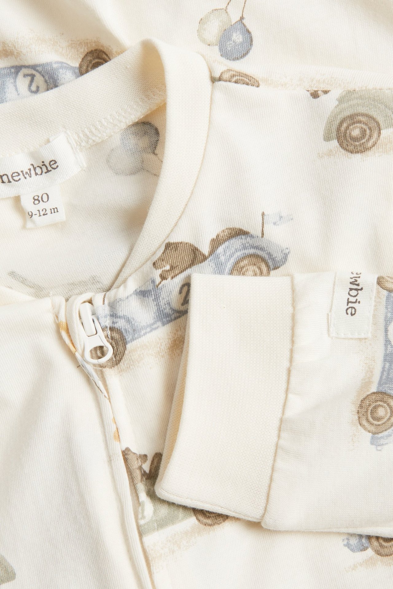 Close-up of offwhite baby pyjamas in soft jersey with bear and car pattern, two-way zipper.