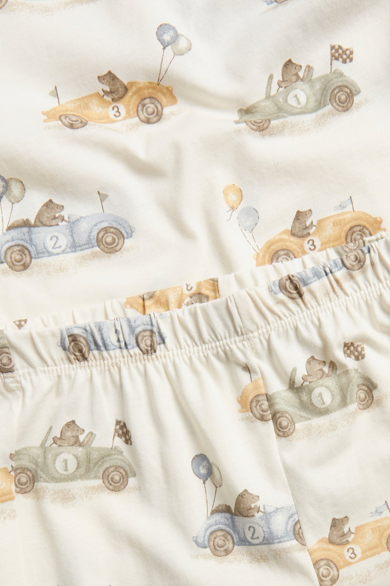 Nahaufnahme von cremefarbenem Baby-Pyjama-Stoff mit Bären in Autos und Ballons-Print, Gummibund.