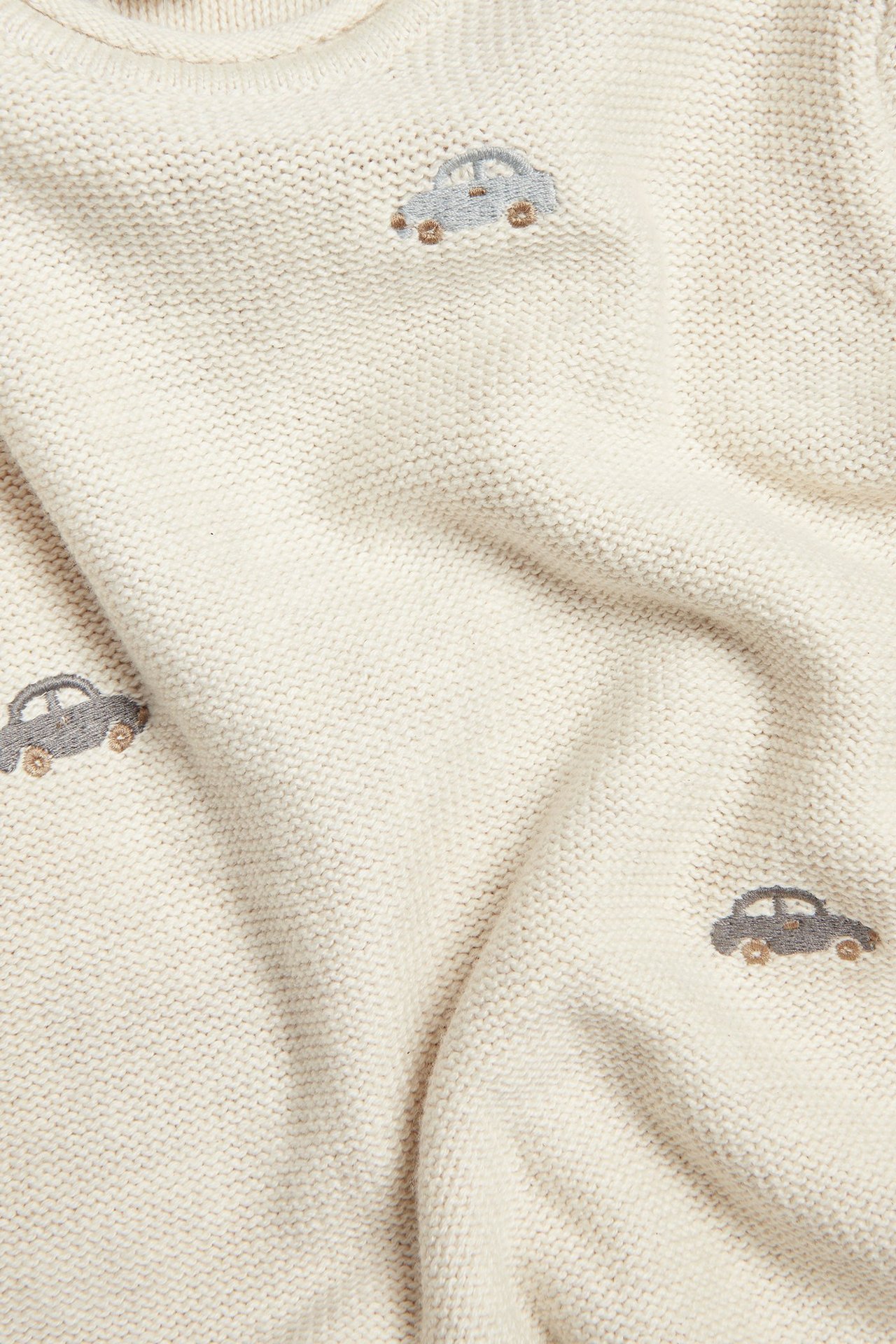 Nahaufnahme eines beigen melierten Baby-Strickpullovers aus Baumwolle mit gestickten blauen und grauen Autos.