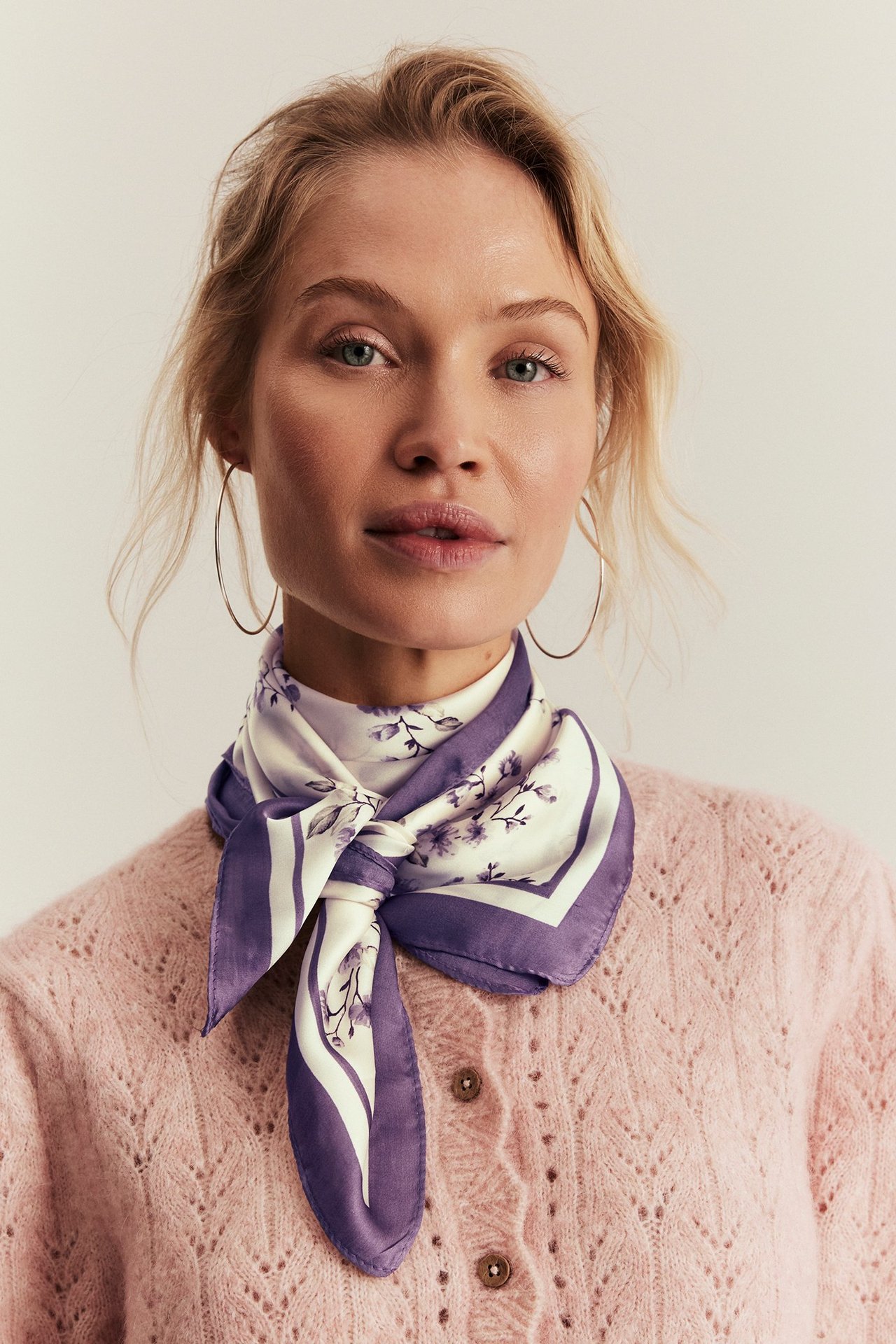 Close-up front view of a woman wearing a light lilac floral polyester scarf and a pink knitted cardigan.