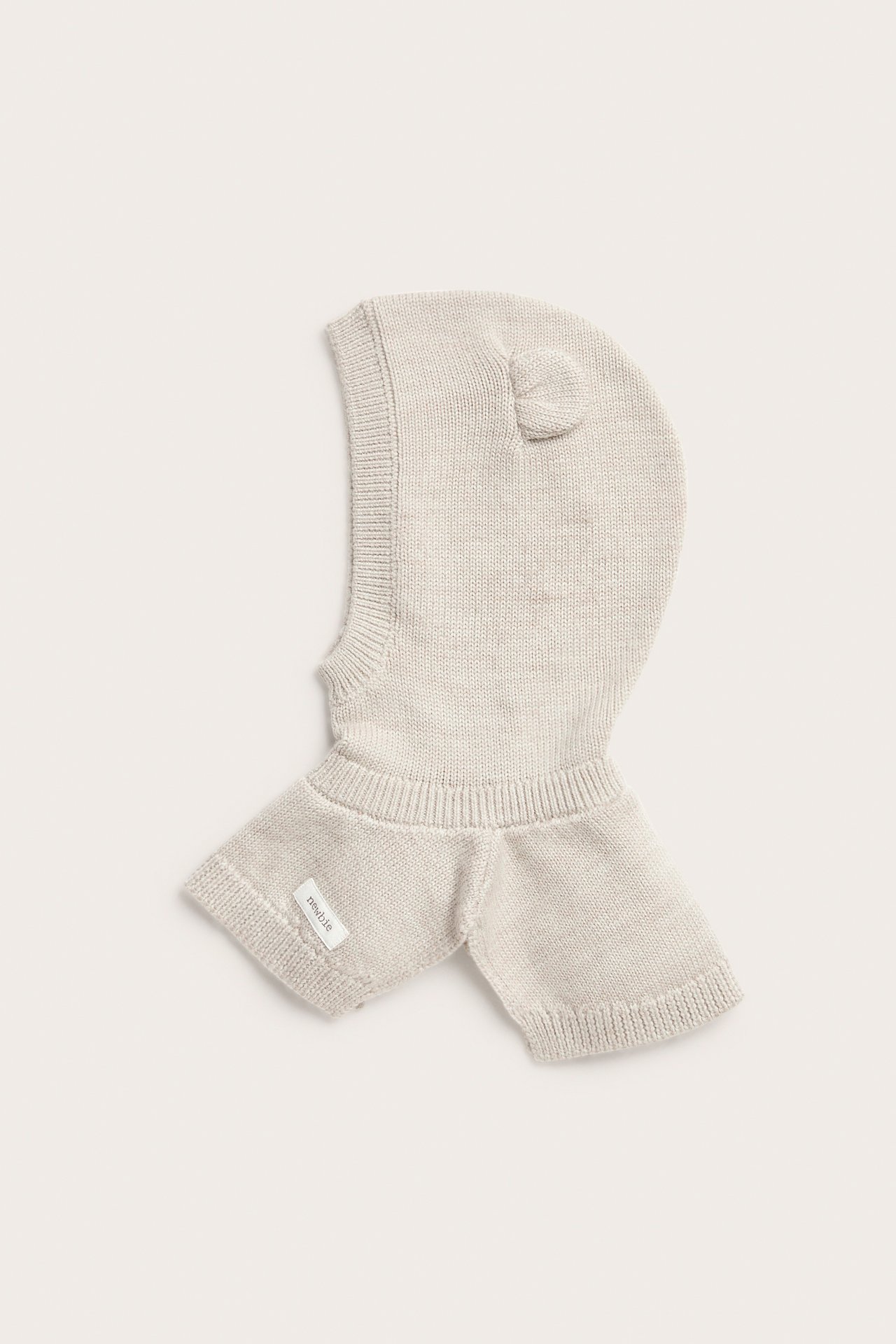 Vorderansicht einer hellbeigen gestrickten Baby-Balaklava mit kleinen Ohren und einem Etikett.
