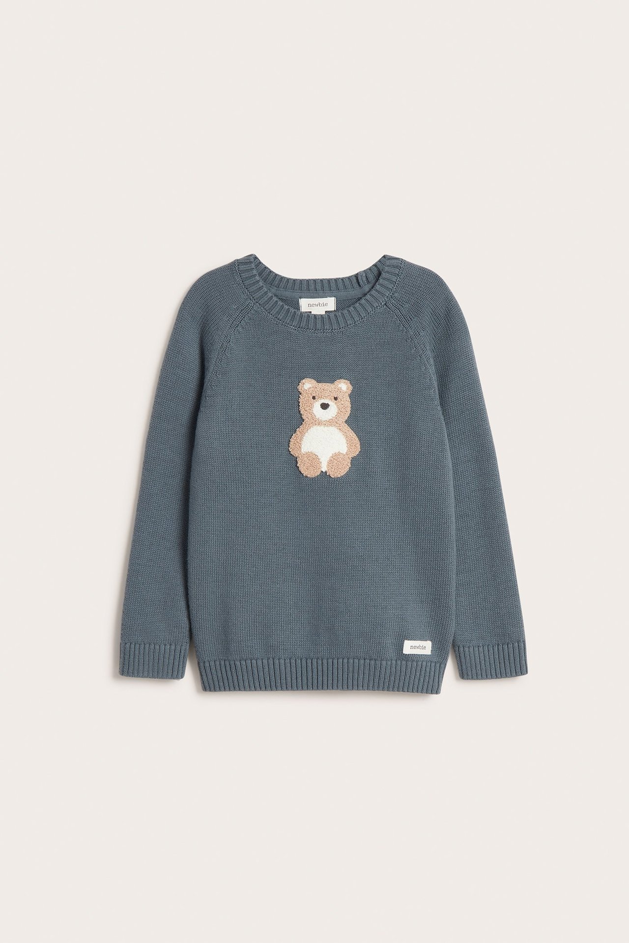 Vorderansicht: Ein blauer Kinder-Baumwollpullover mit einer strukturierten beigen Bärenapplikation.