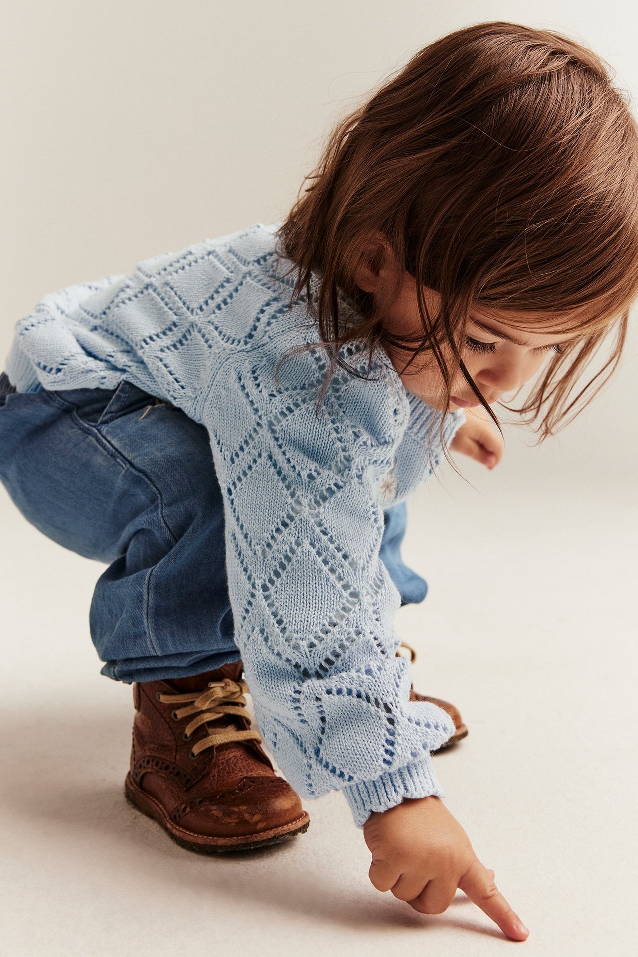 Nahaufnahme eines Kindes in hellblauer gemusterter Strickjacke, blauen Jeans und braunen Stiefeln.