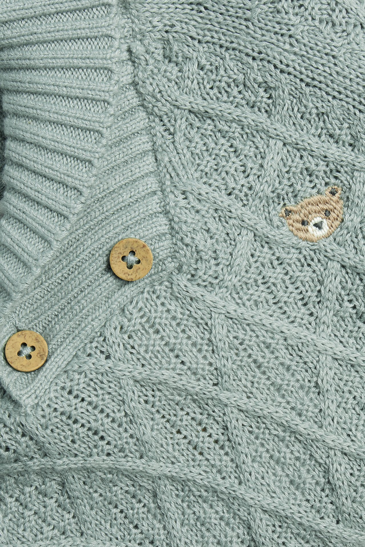 Close-up front view: Light green knitted cotton cardigan with cable knit, wooden buttons, and embroidered bear.