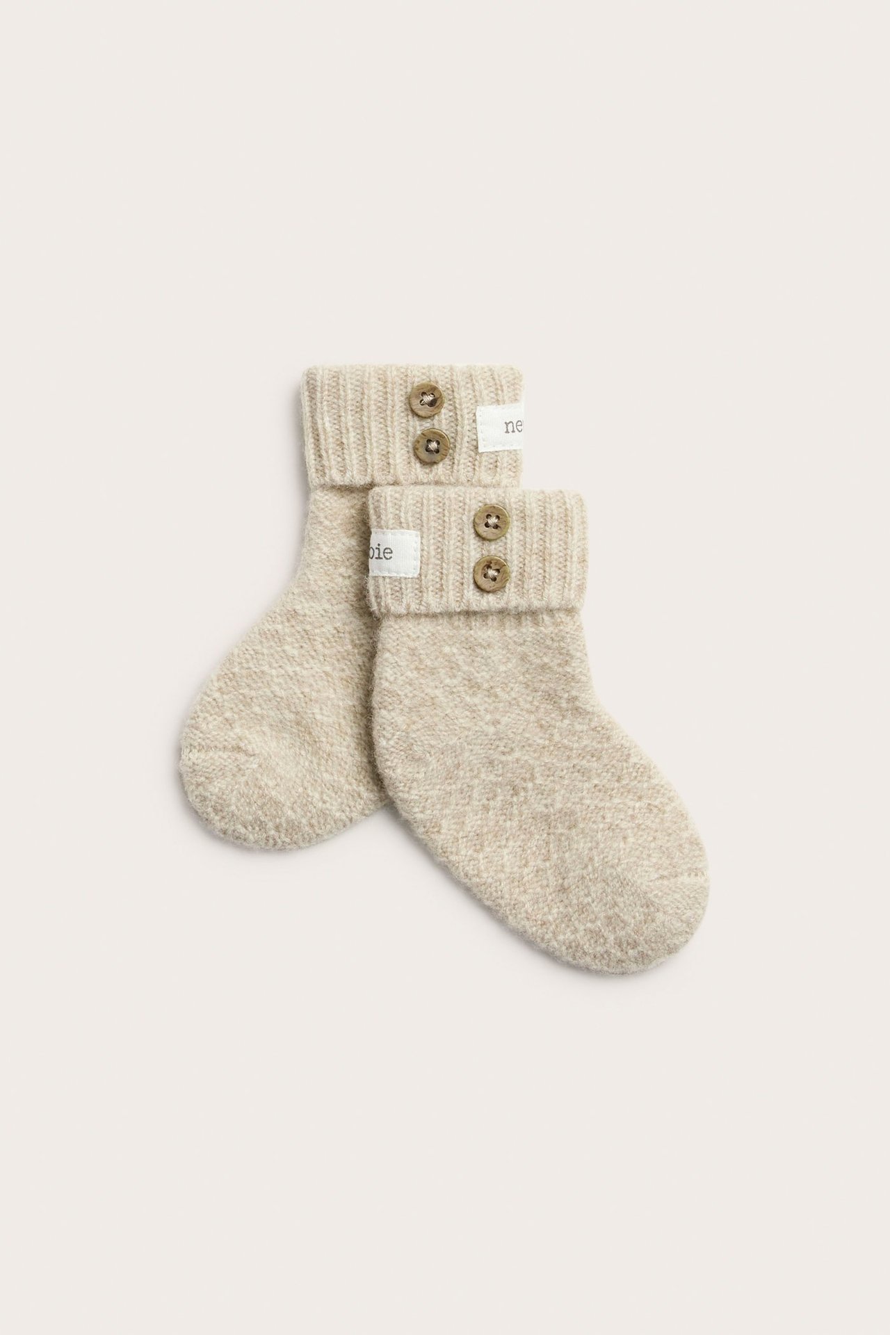 Top view of beige melange baby booties with ribbed foldable cuffs, two brown buttons, and a Newbie label.