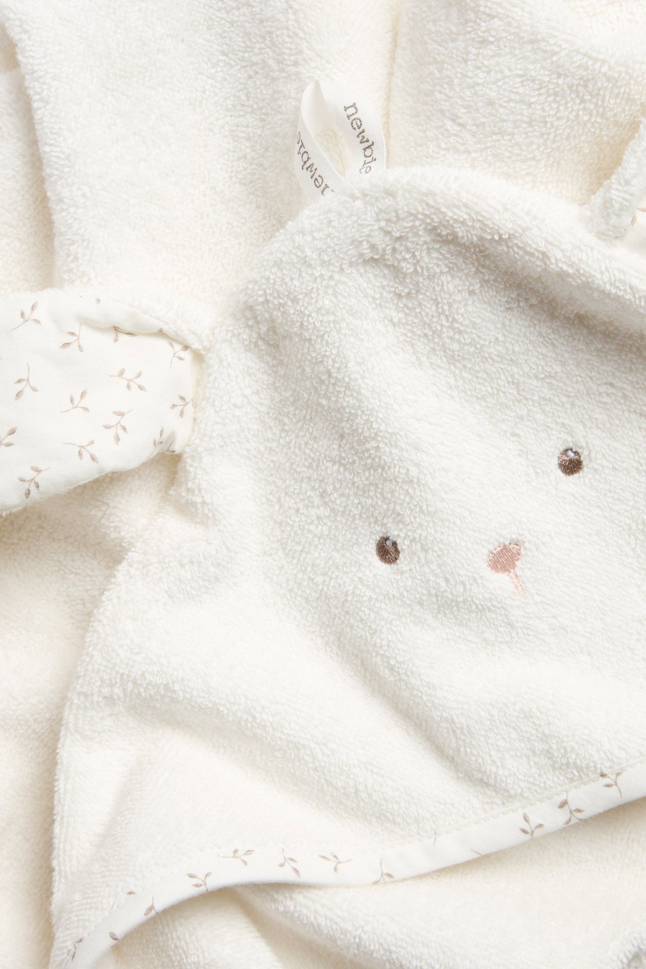 Close-up of an offwhite terry baby hooded towel with bunny ears, embroidered face, and patterned trim.