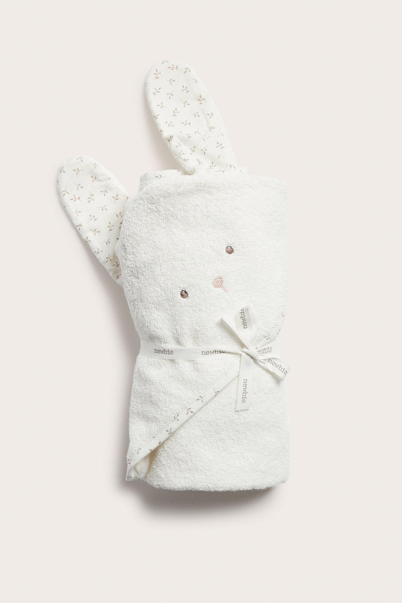 Front view: Off-white cotton terry hooded baby towel with embroidered rabbit face and printed ears, tied with a ribbon.