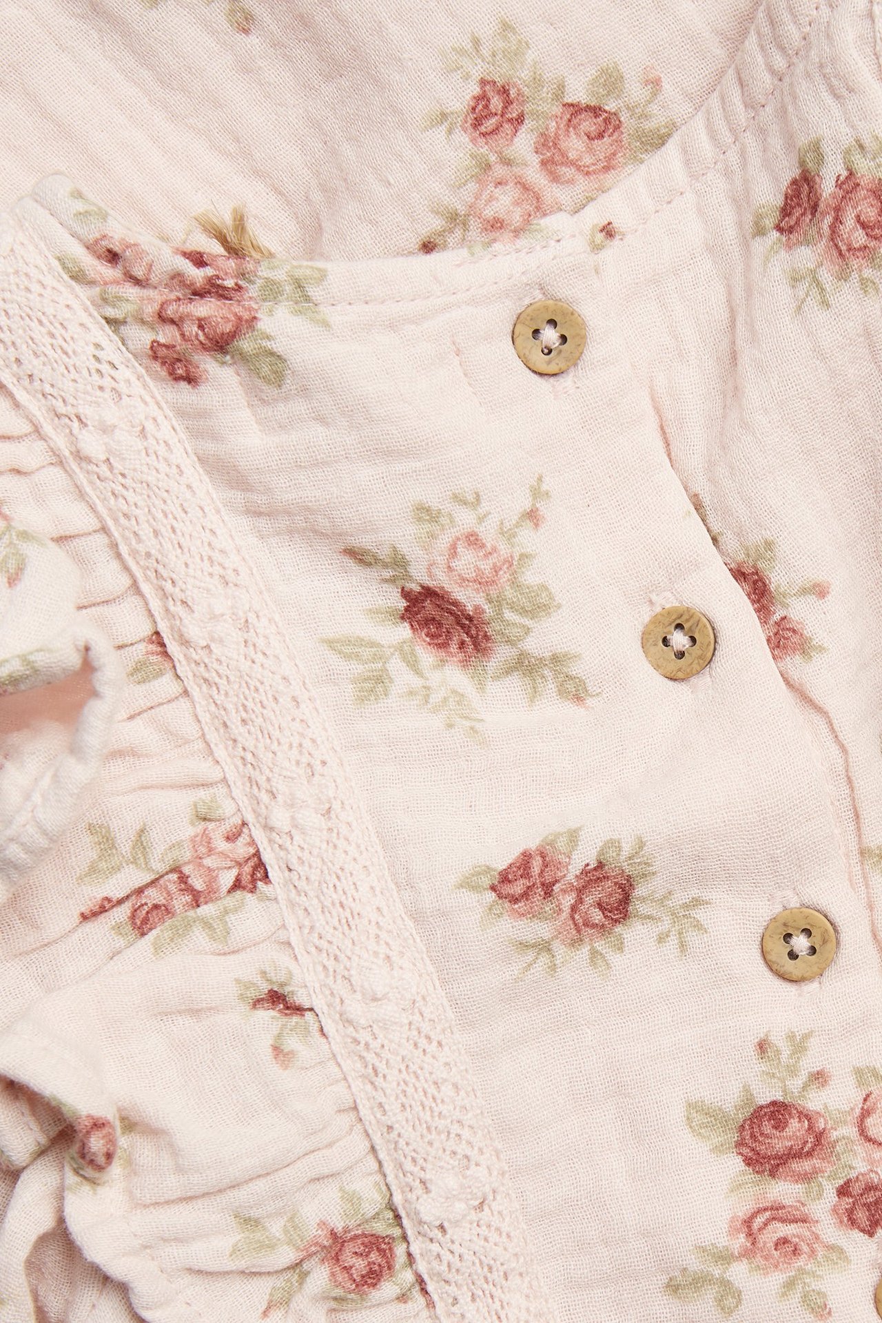 Close-up of a light pink floral ruffled dress with wooden buttons and lace trim.