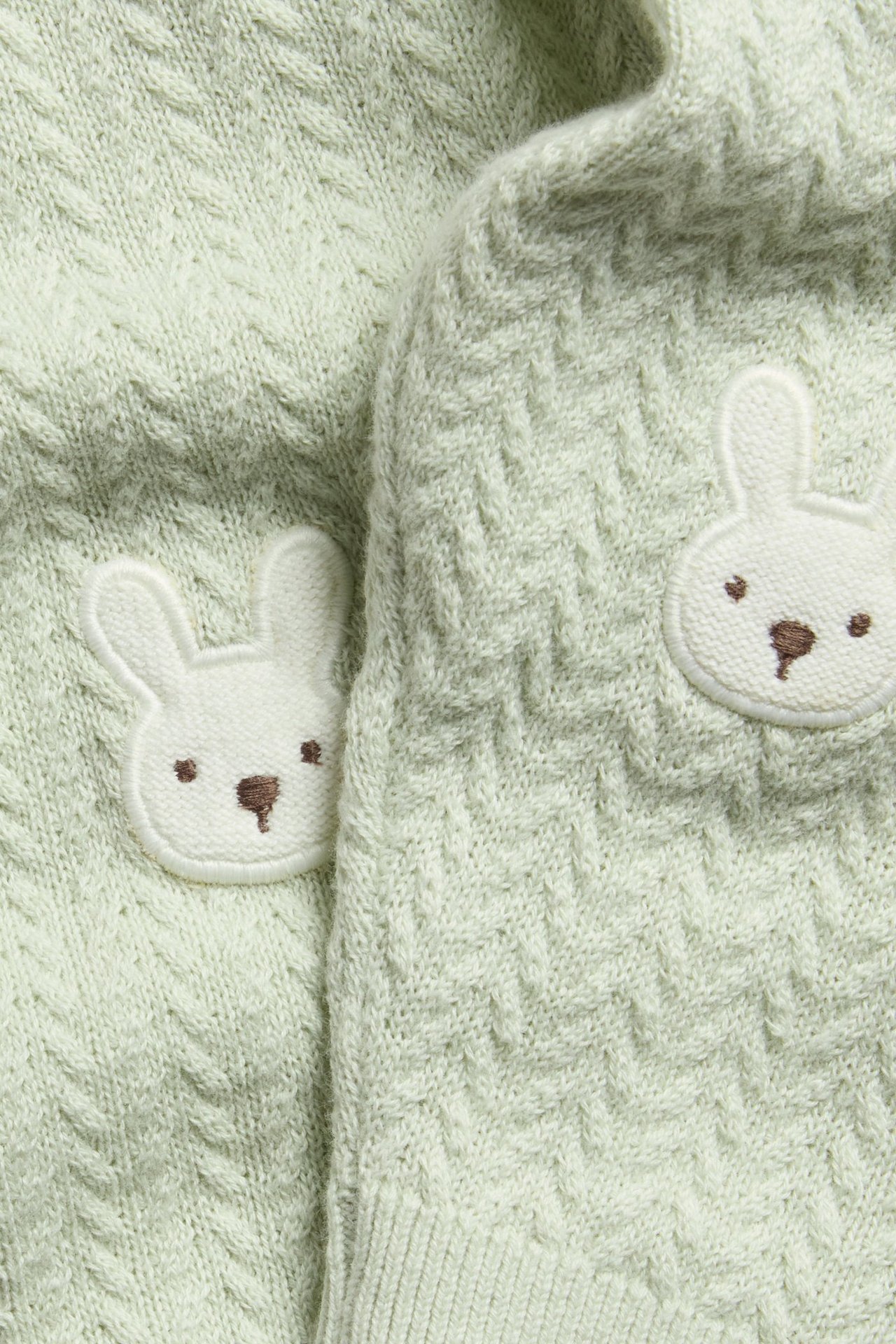 Close-up of light green structured knit baby leggings with white bunny embroidery on the knees.