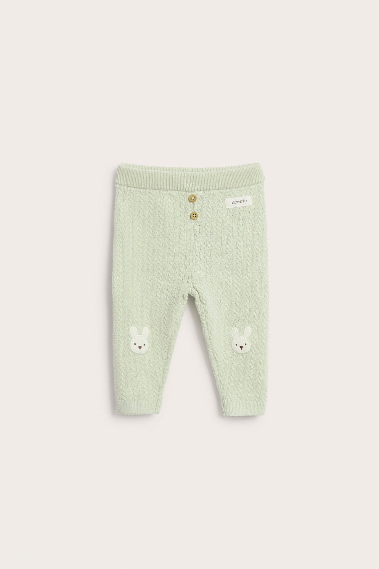 Front view of light green structure-knitted baby leggings with decorative buttons and bunny embroidery on the knees.