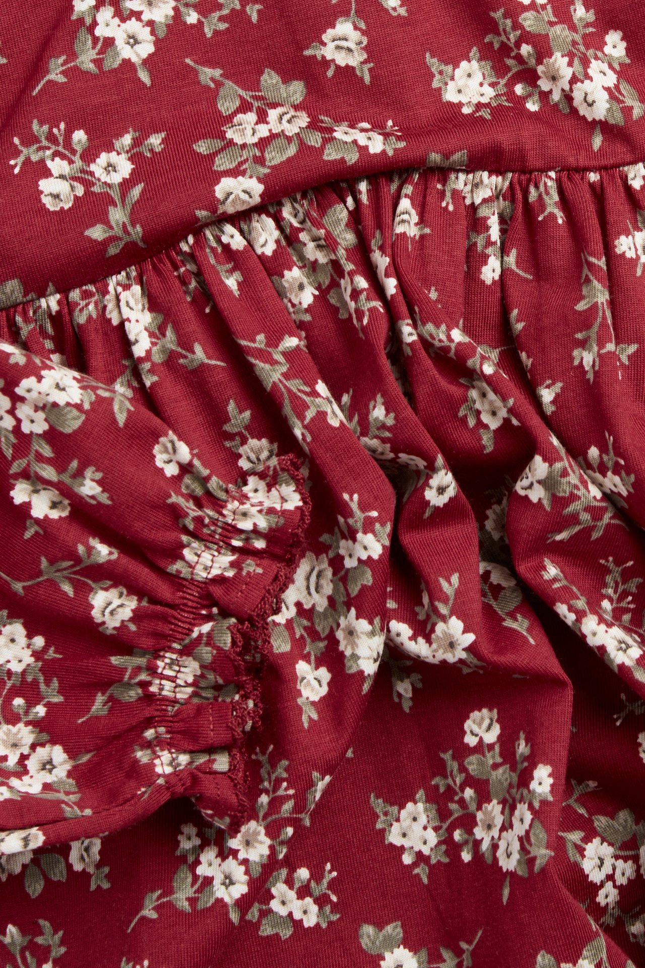 Close-up: red floral jersey dress with white flowers, gathered seam, elasticated puff sleeve.