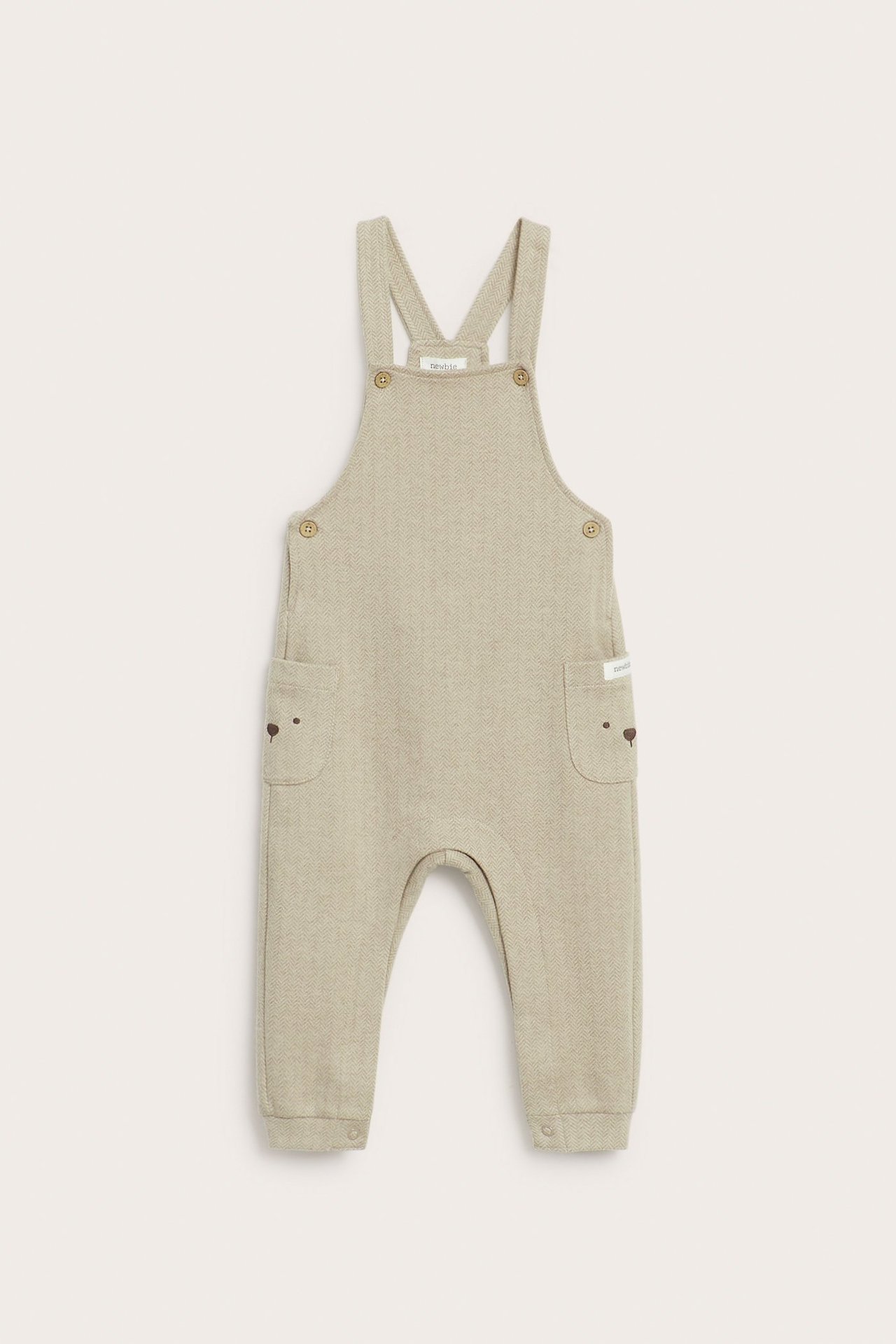 Front view of beige melange baby overalls with herringbone pattern, buttoned straps, side pockets with bear embroidery.