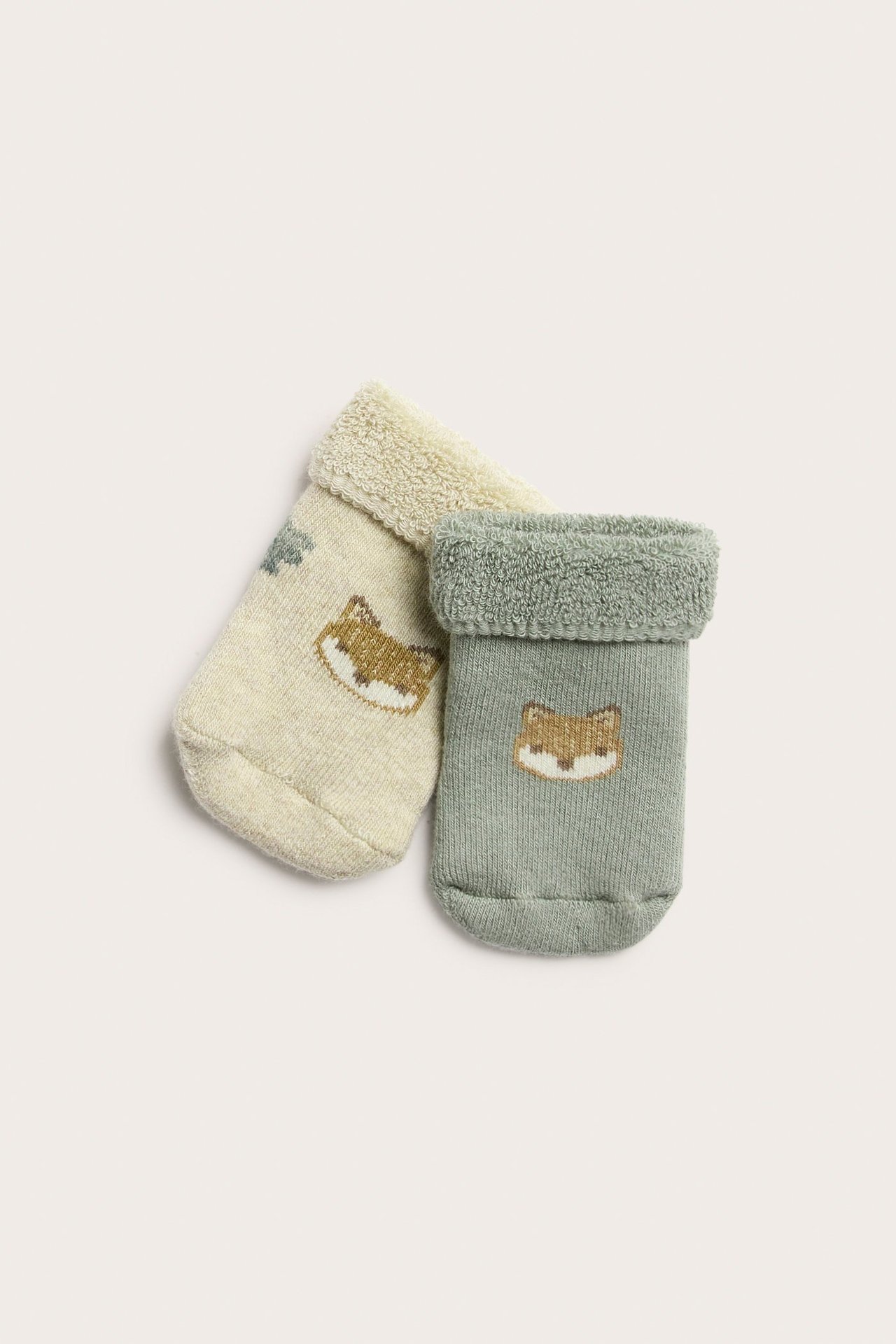 Nahaufnahme von zwei Kinder-Frotteesocken, eine dunkelgrün, eine hellbeige, beide mit Fuchsmuster.