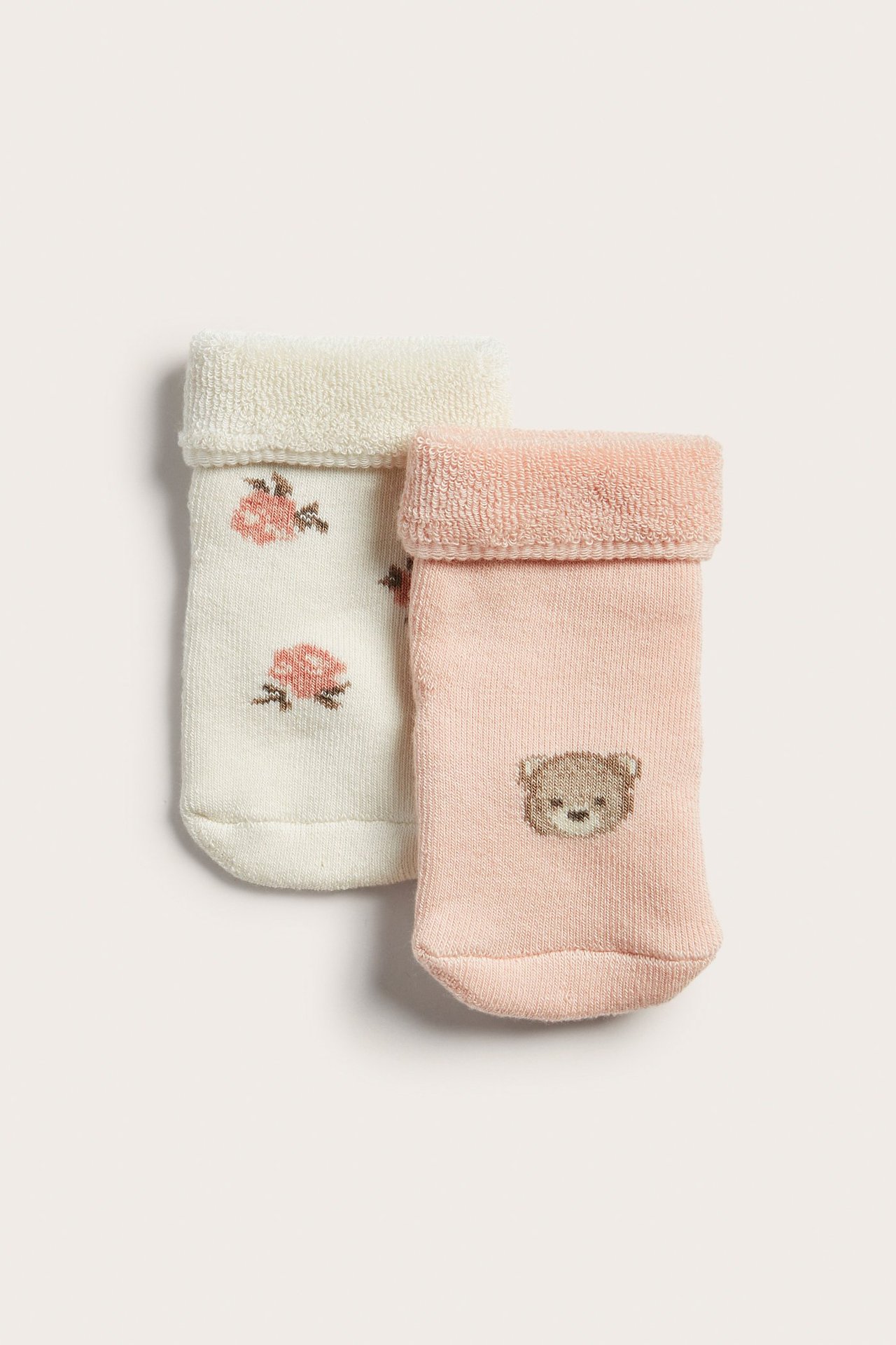 Nahaufnahme von zwei Paar Baby-Frotteesocken: hellrosa mit Teddybär, cremefarben mit Rosenmuster.
