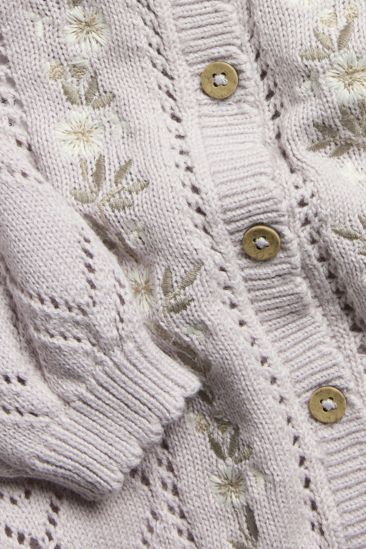 Close-up of a light lilac pattern-knitted cotton cardigan with white floral embroidery and wooden buttons.