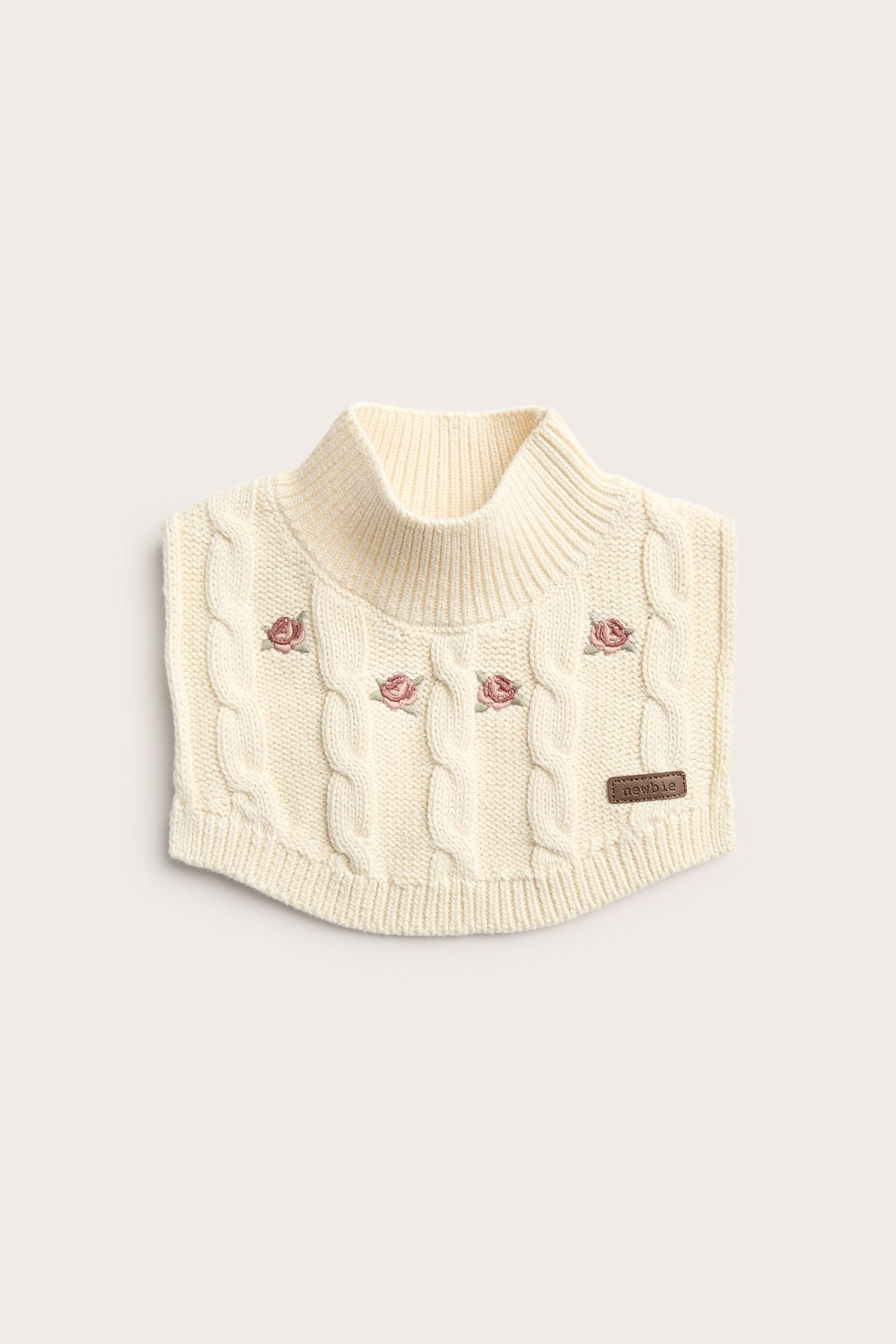 Vorderansicht eines baby hellbeigen Strick-Falschrollkragens aus Baumwolle mit Zopfmuster und rosa Rosenstickerei.