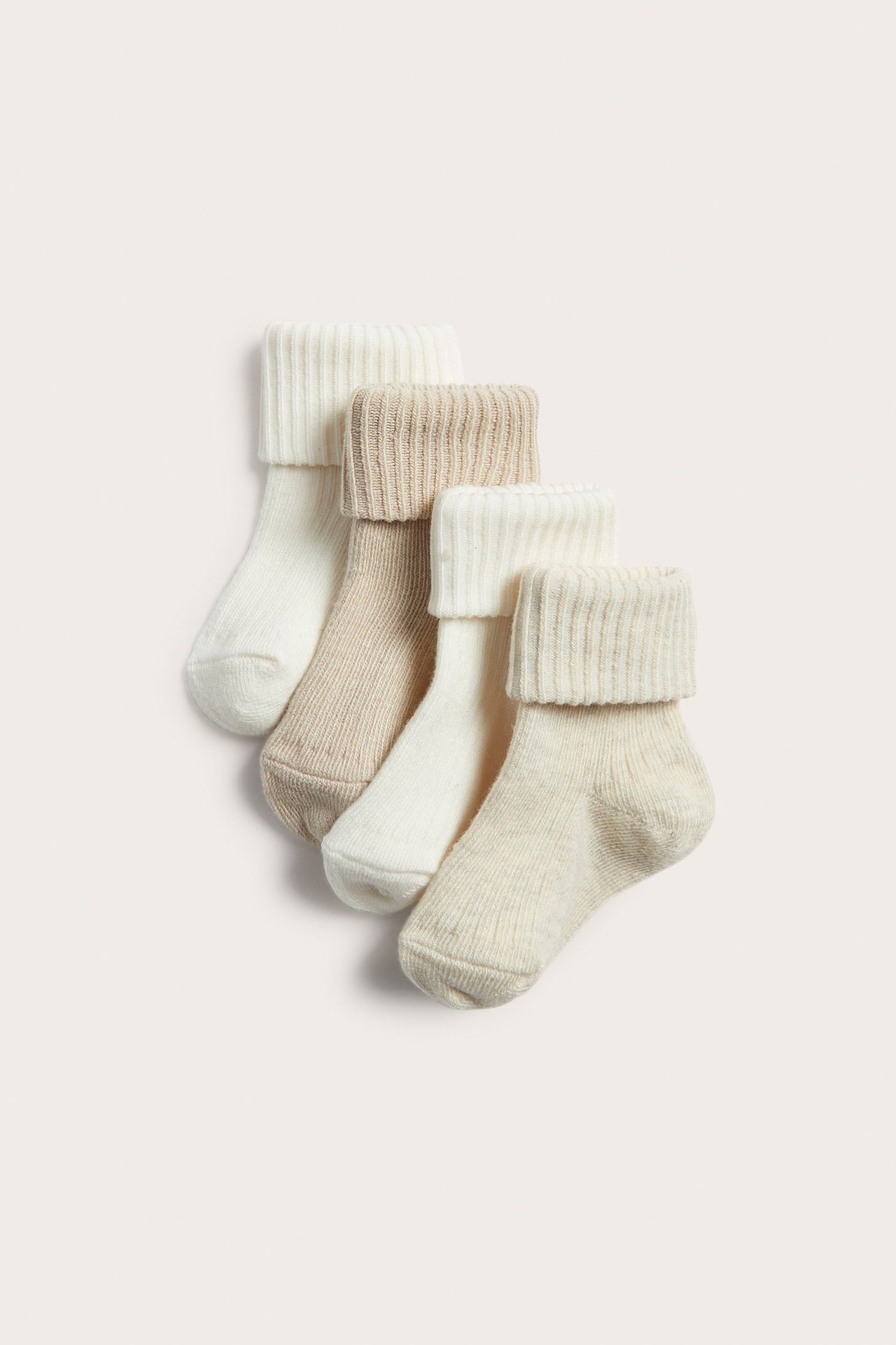 Nahaufnahme von vier Paar gerippten Babysocken in Hellbeige und Off-White mit umgeschlagenen Bündchen.
