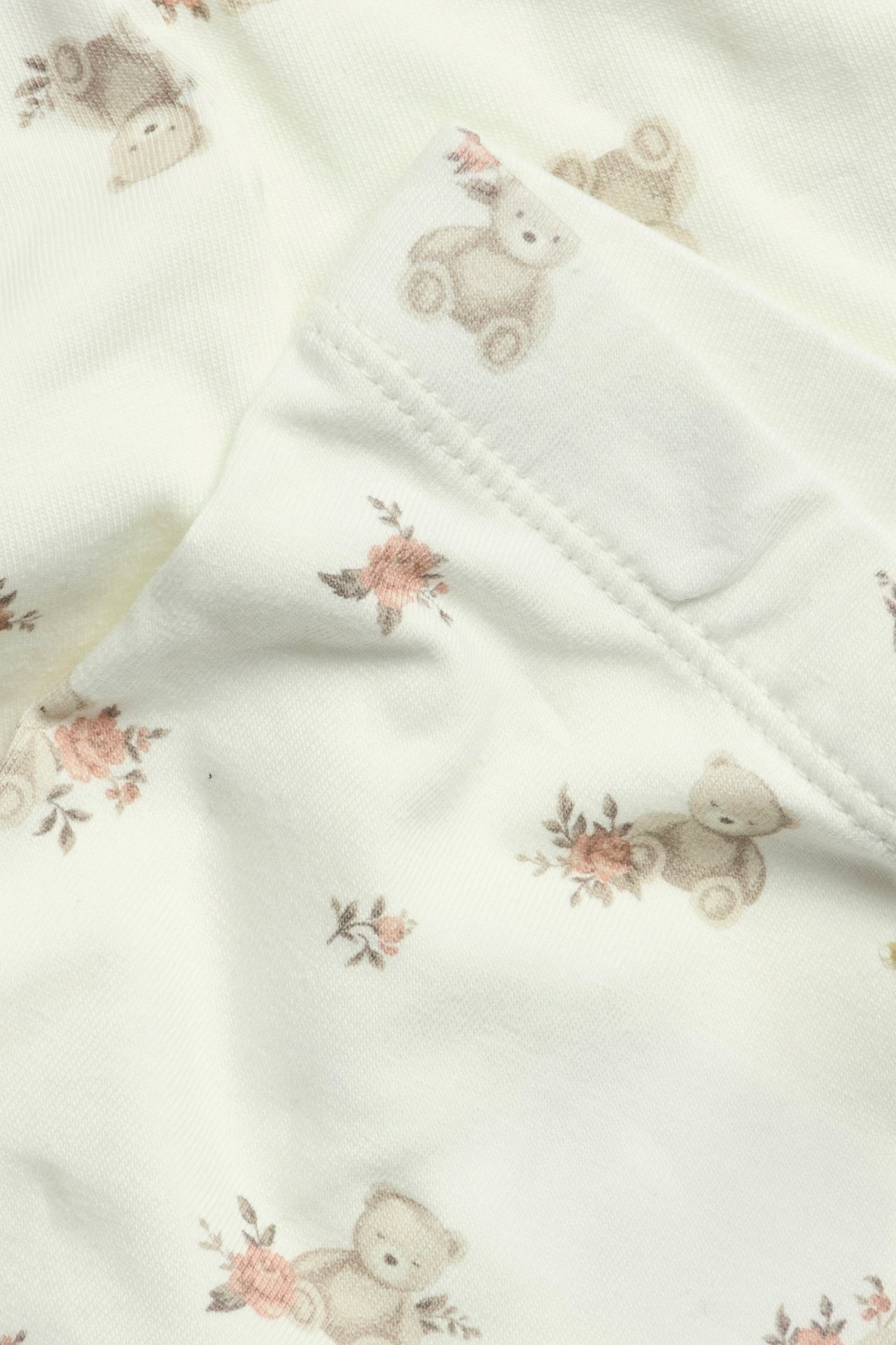 Nahaufnahme von cremefarbenen Baby-Leggings mit Bären- und kleinen Blumenmuster.