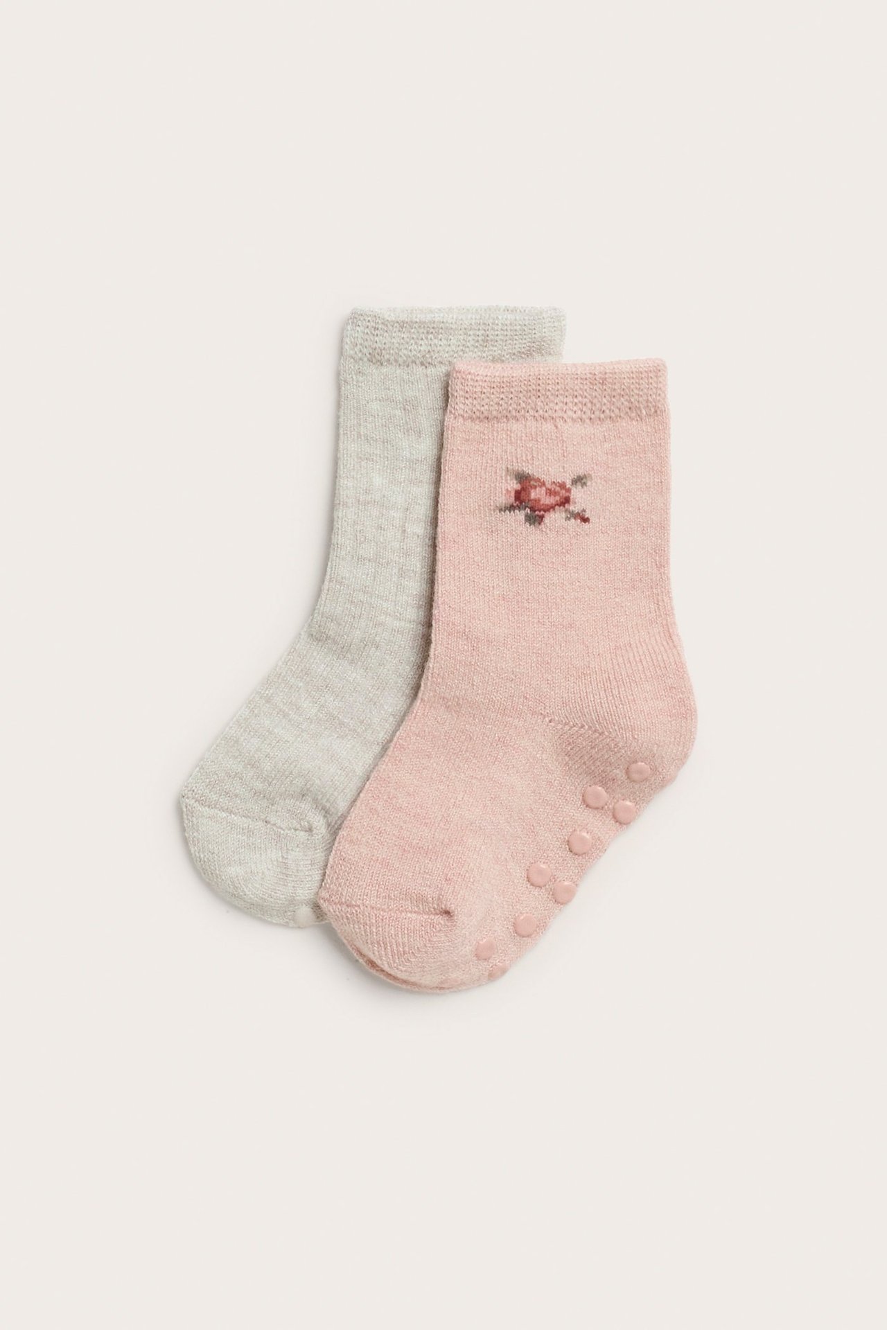 Draufsicht auf zwei Baby-Wollmixsocken: eine hellrosa mit Blume und Antirutsch, eine hellgraue.