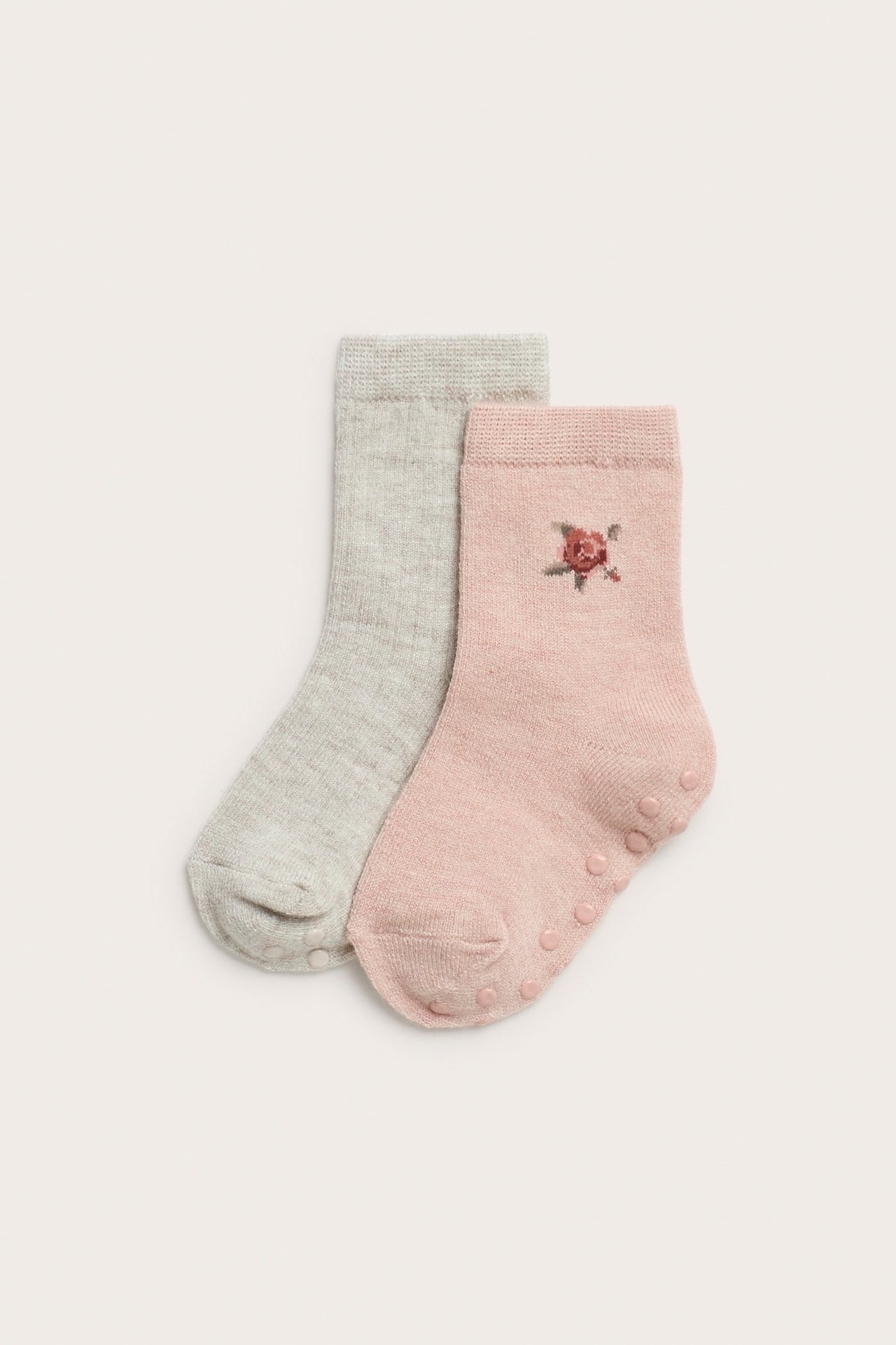 Nahaufnahme von zwei Paar Baby-Wollmixsocken: hellrosa mit Blume, hellgrau, beide mit Antirutsch-Noppen.