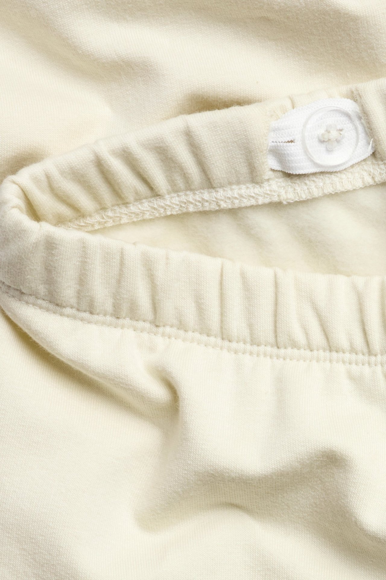Nahaufnahme des hellbeigen Baumwoll-Leggingsbunds mit verstellbarem Gummizug und weißem Knopf.