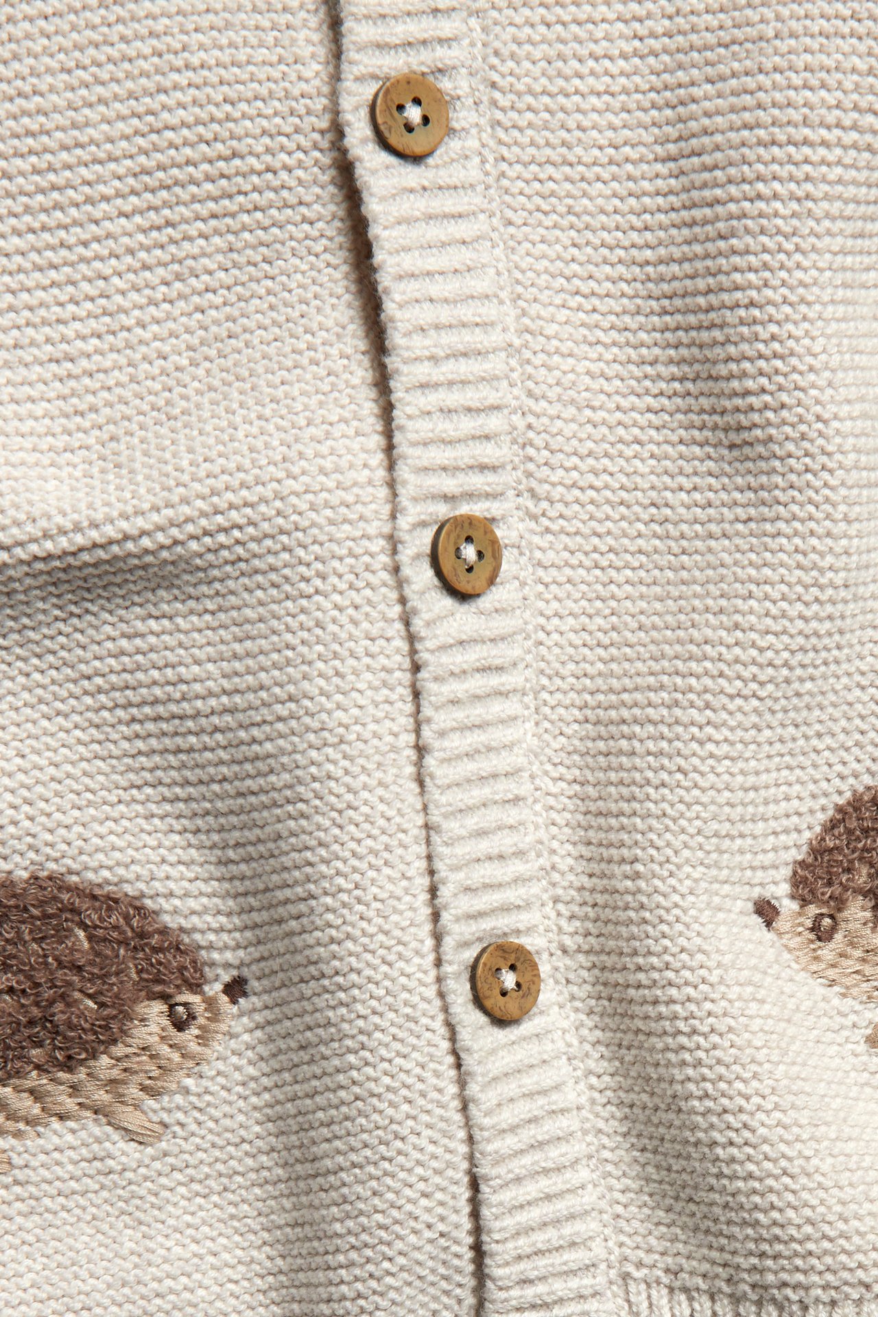 Close-up front view of a beige melange knitted baby cardigan with hedgehog embroidery and wooden buttons.