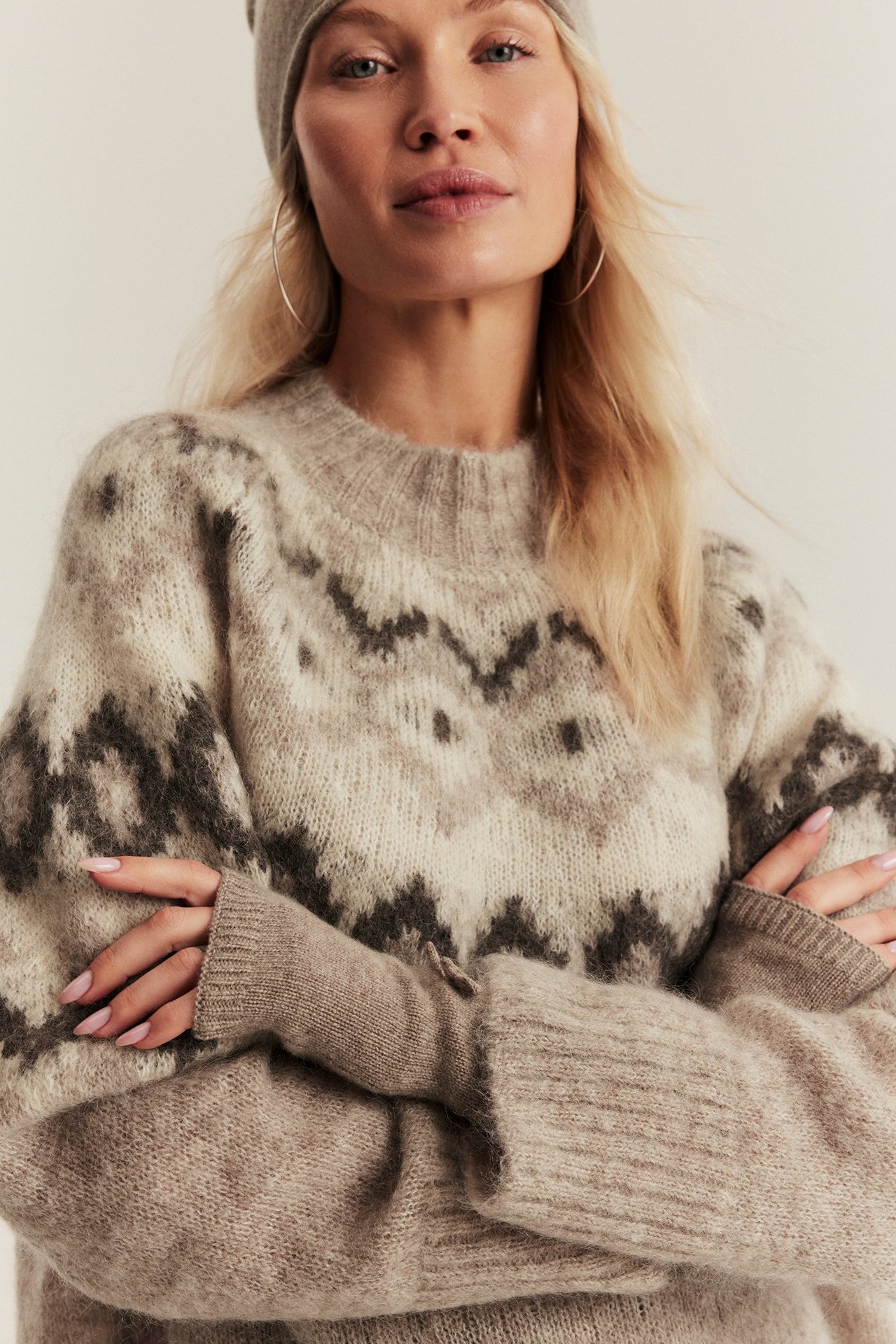Front view of a woman wearing solid beige melange wool cashmere wrist warmers with a patterned sweater.